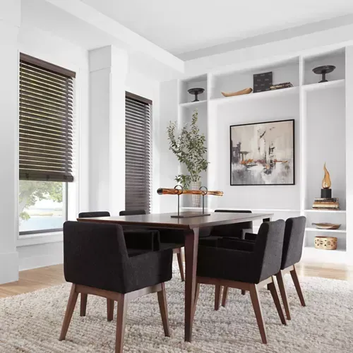 Dining room with dark wood table, black chairs, and built-in shelves. Large abstract painting and light-colored rug.