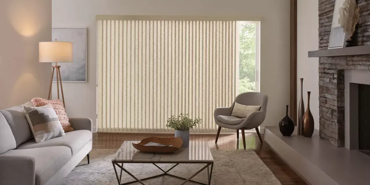 Living room with vertical blinds, a light-colored sofa, armchair, coffee table, fireplace, and artwork.