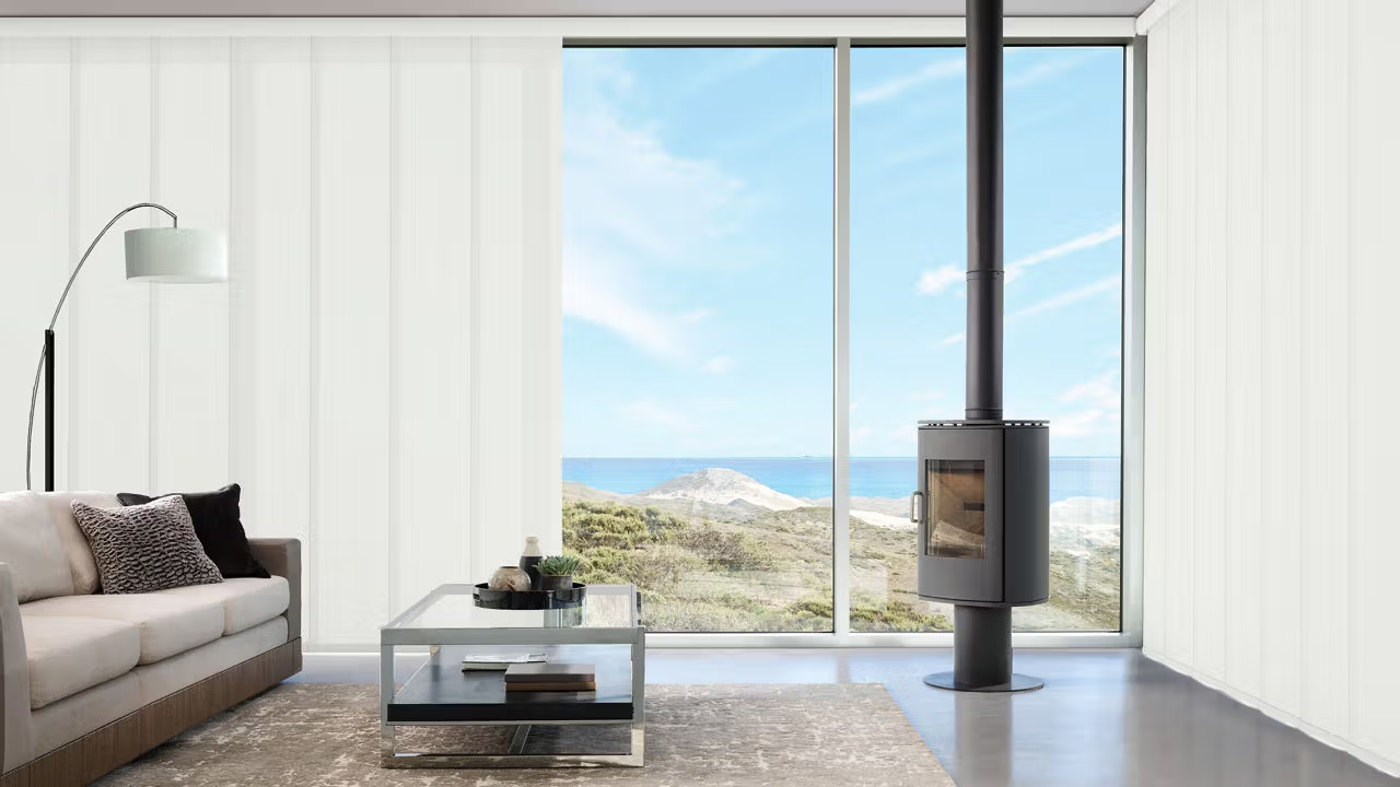 Modern living room with a beach view, featuring white vertical blinds, a gray sofa, and a fireplace.