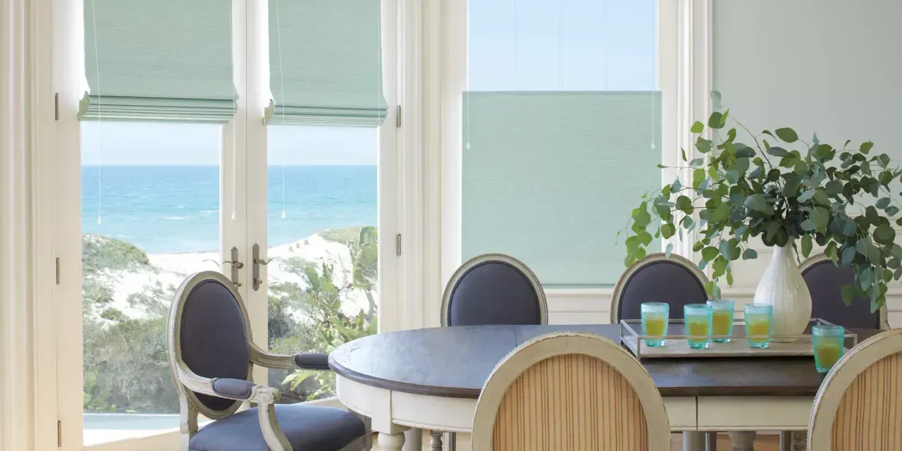 Dining room with ocean view. A table is set with a centerpiece and drinks, framed by windows with blue views and white trim.