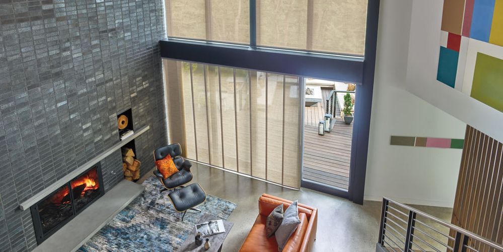 An overhead view of a modern living room with a fireplace, seating, and large windows leading to a patio.  The walls are dark brick and white with colorful art.