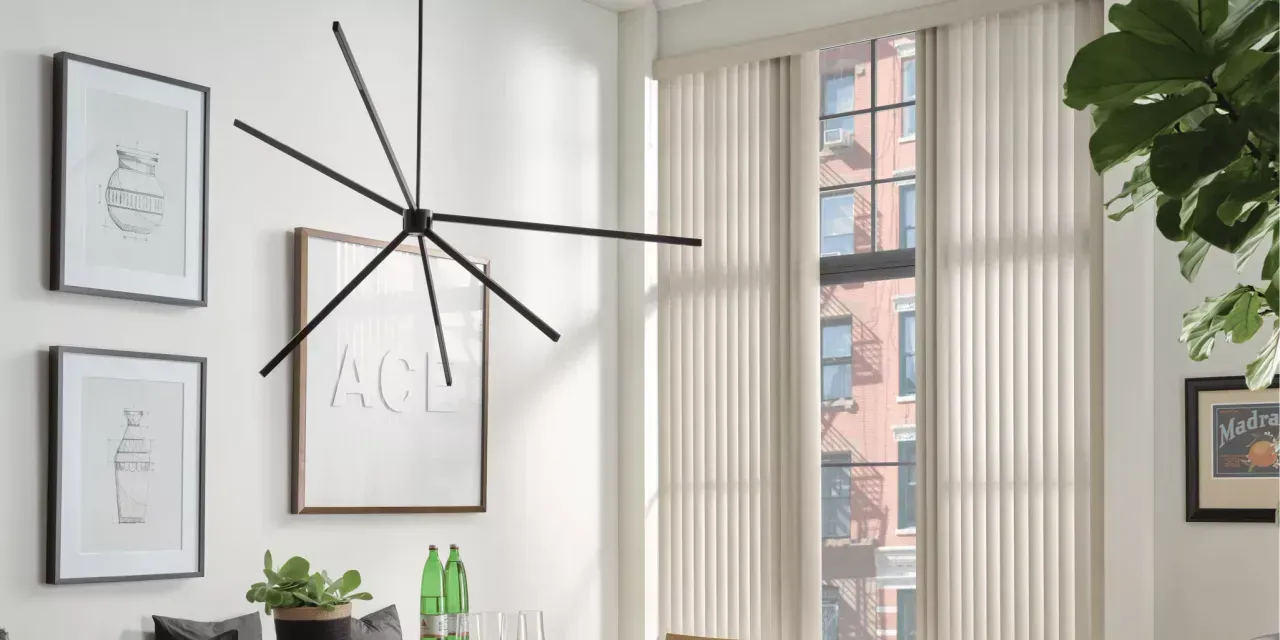 A modern room with artwork, a large chandelier, and sheer vertical blinds covering a window with a city view.