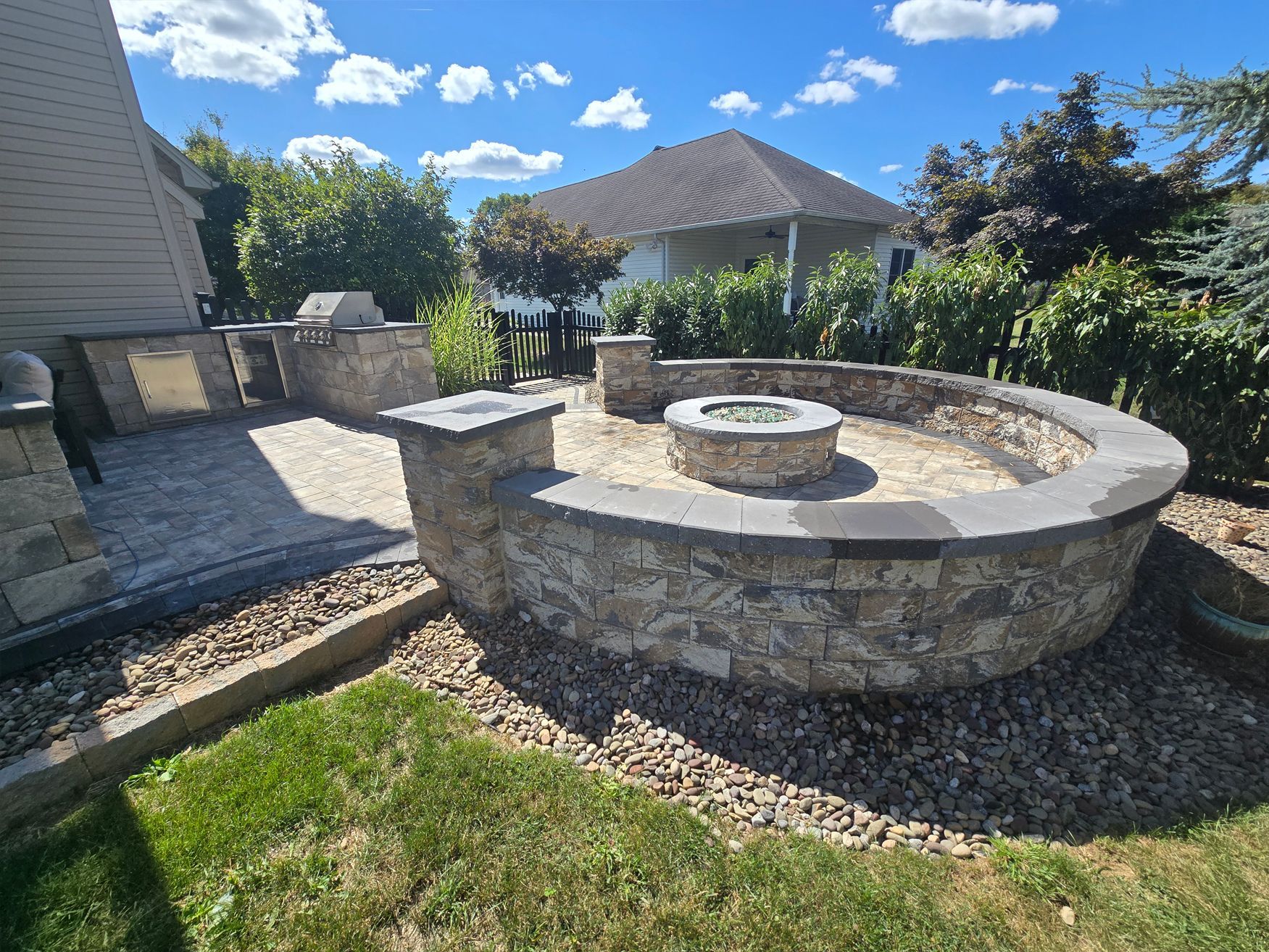 Stone fire pit in a backyard with a patio and grill.