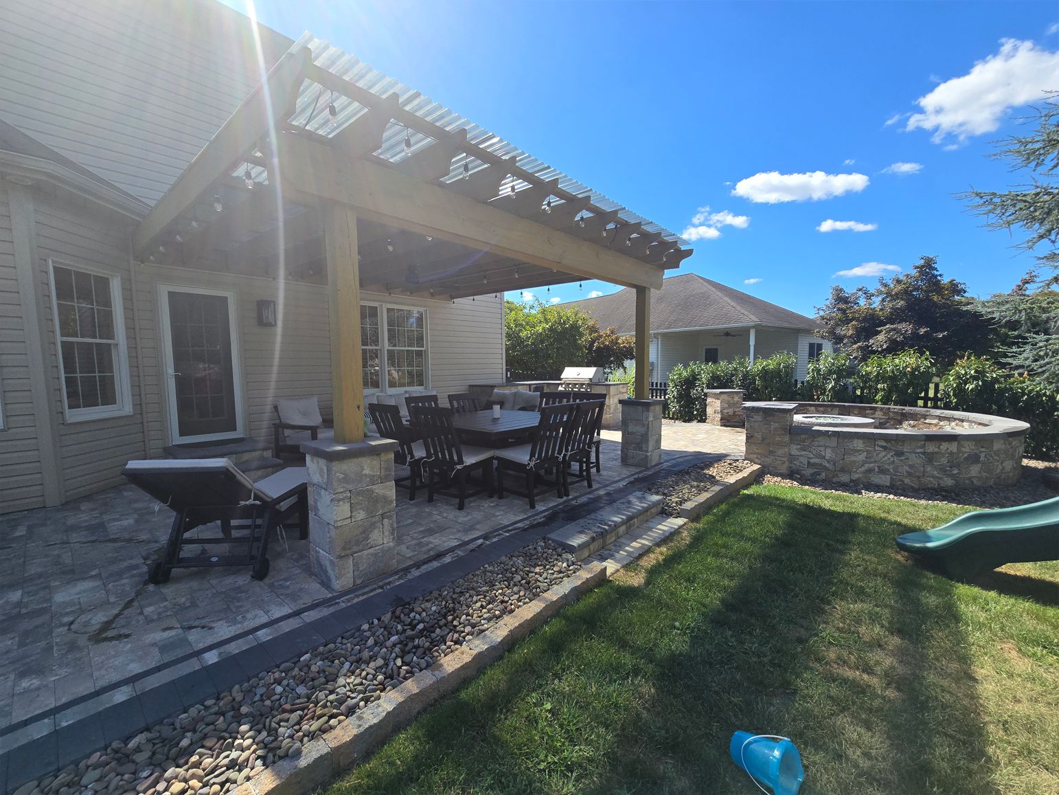 Patio with pergola, stone fireplace, and dining set on a sunny day.