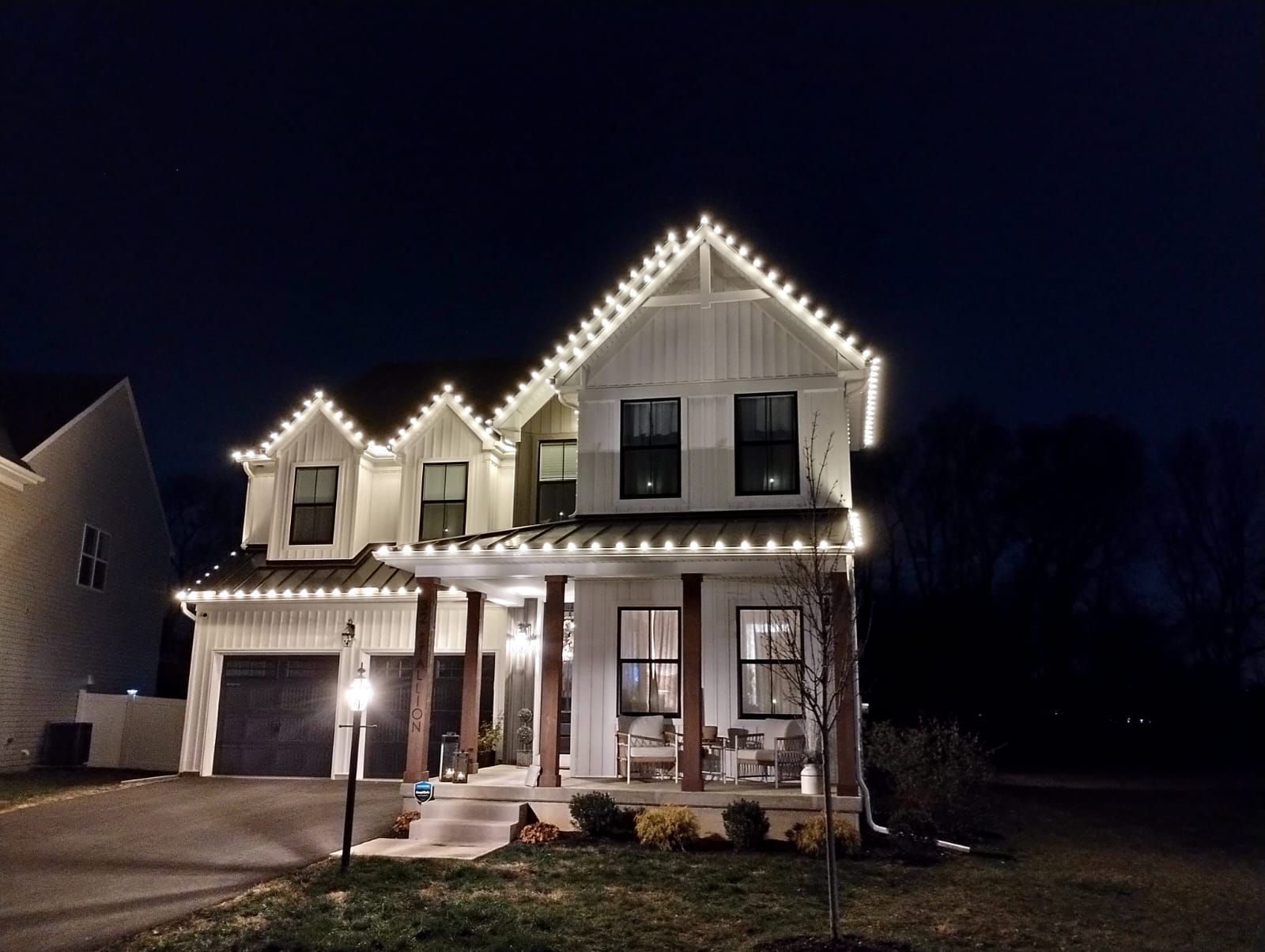 A white house at night with lit white Christmas lights outlining the roof and porch.