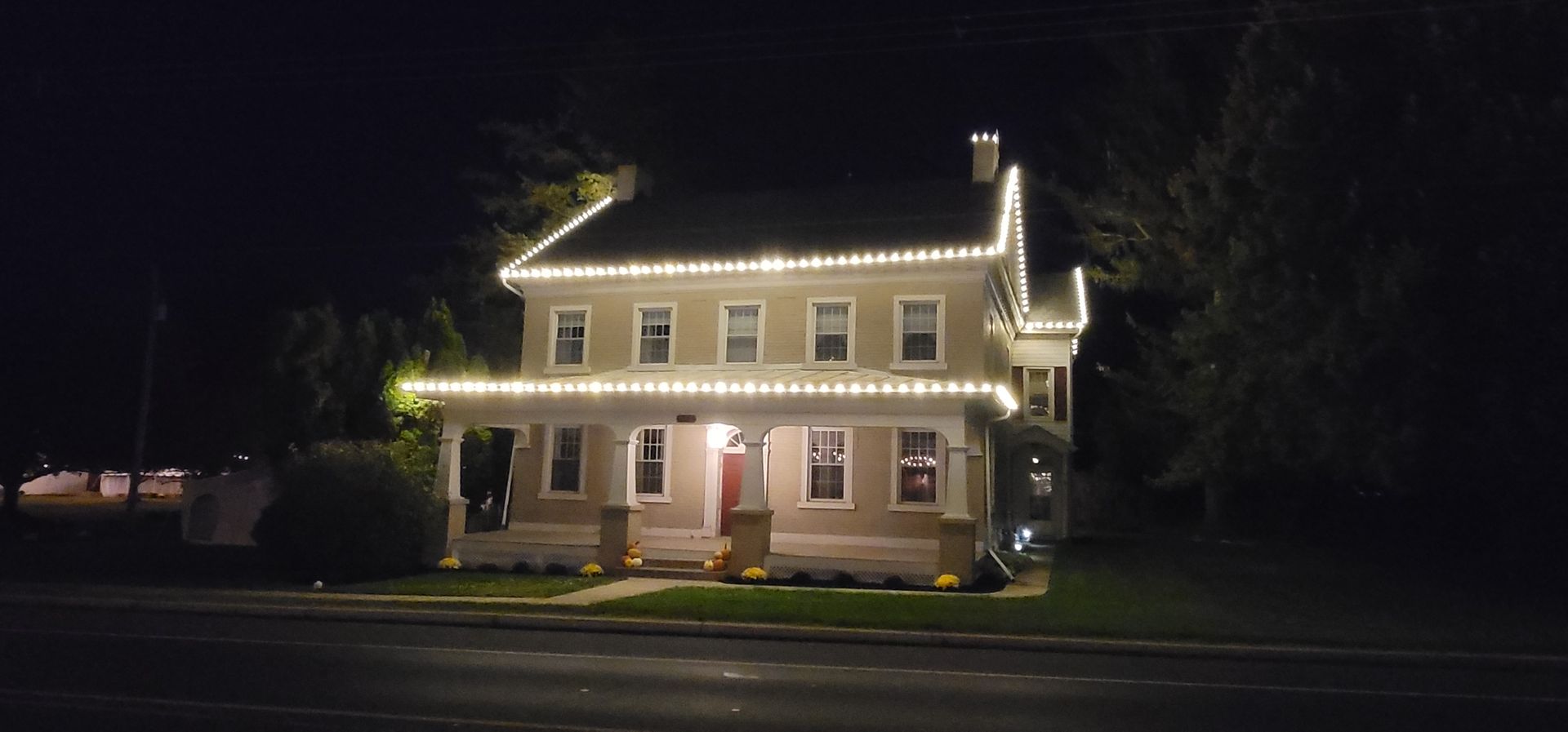 A two-story house at night with Christmas lights outlining the roof and porch.