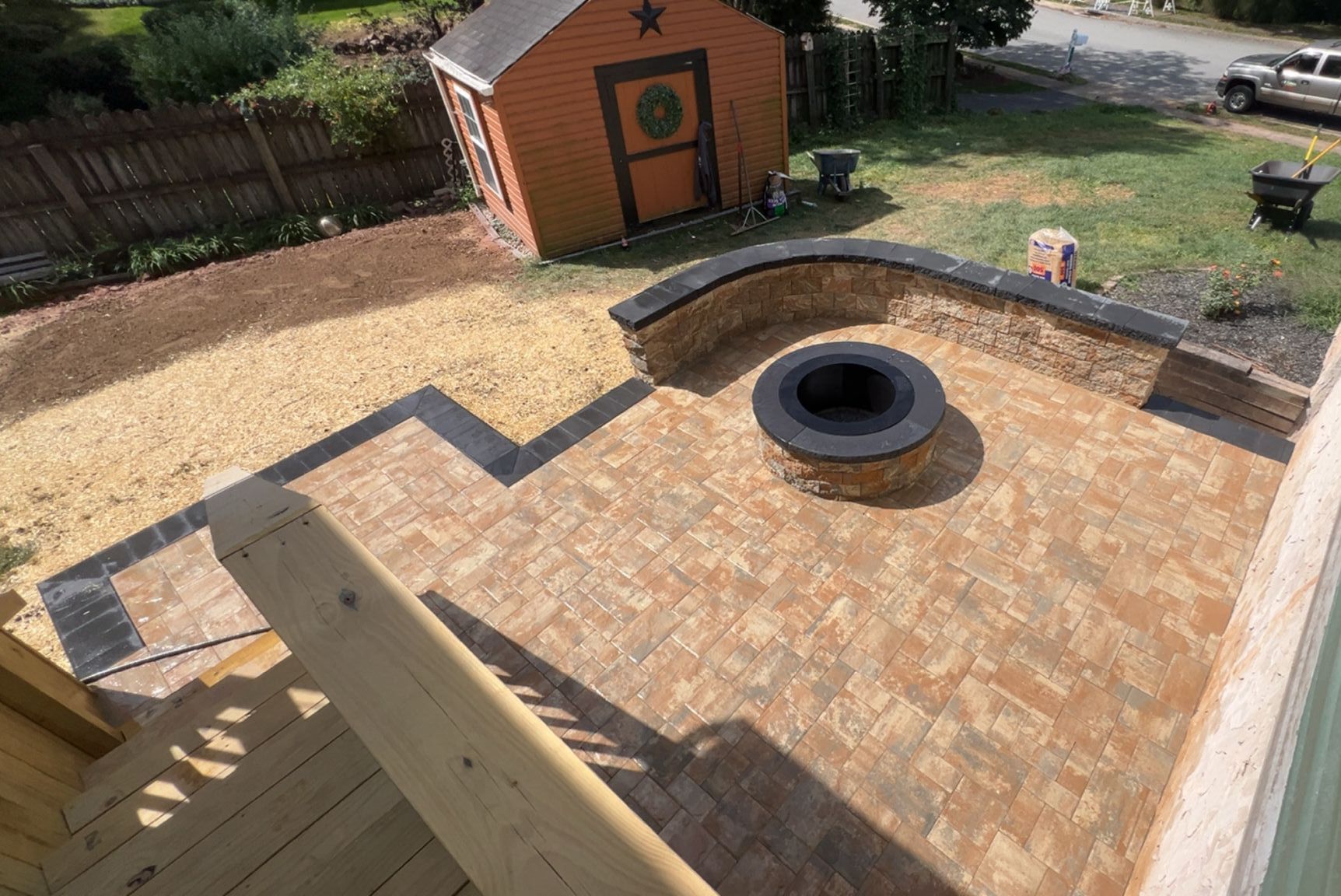 Brick patio with fire pit, steps, and shed in backyard. Brown, orange, and gray colors.