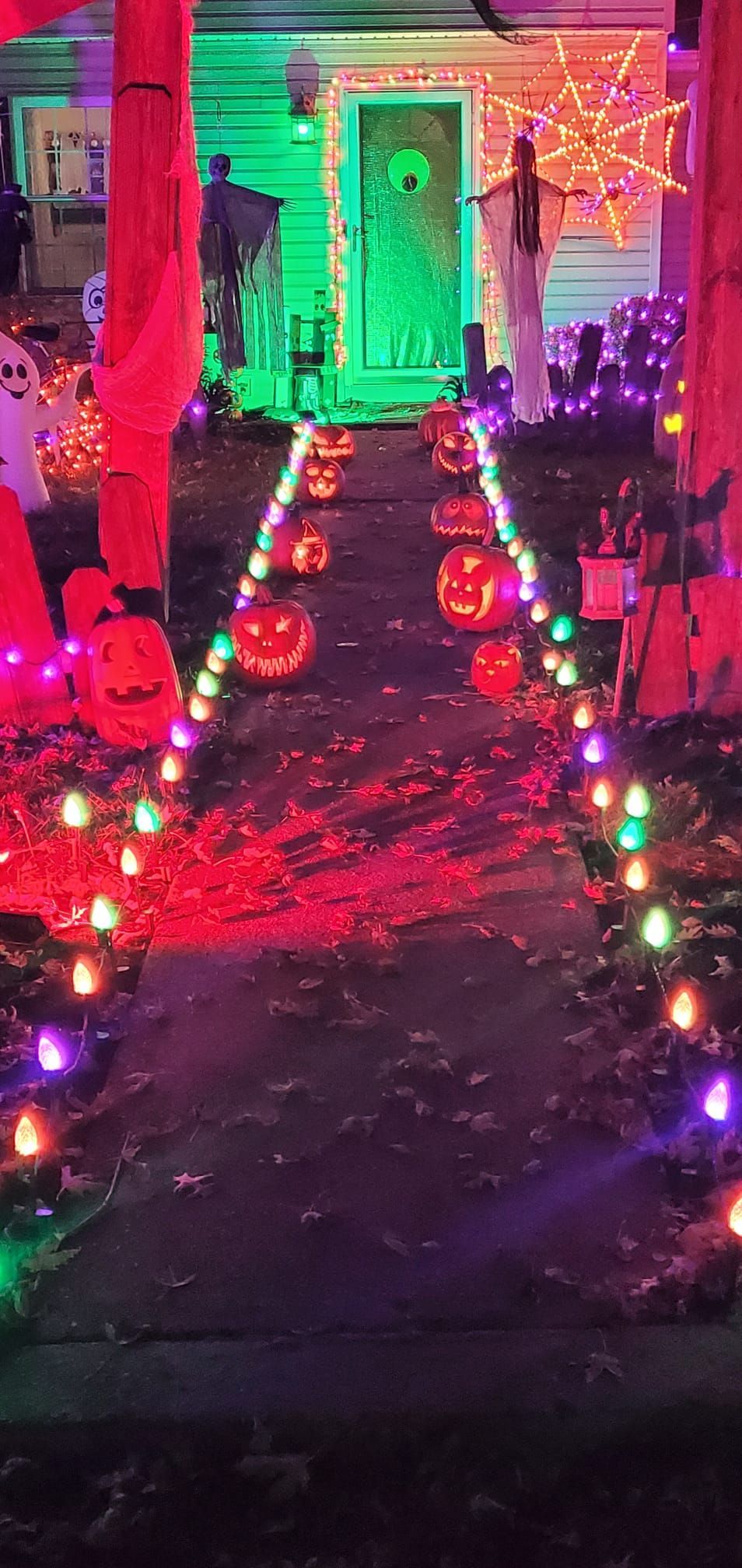 Halloween decorations line a pathway to a house with green and orange lights.