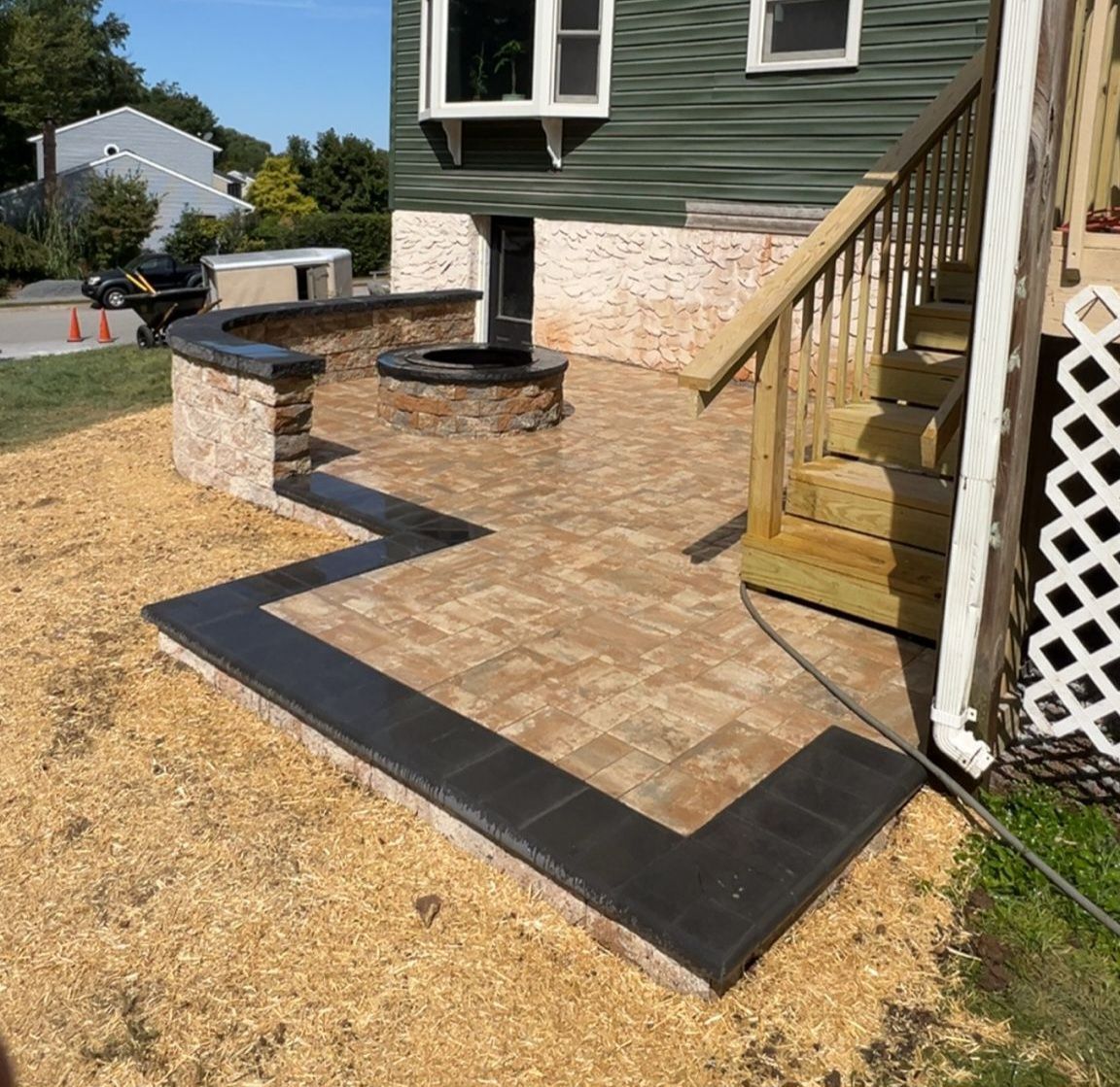Patio with fire pit and stairs next to a green house. Brick walkway with black border.