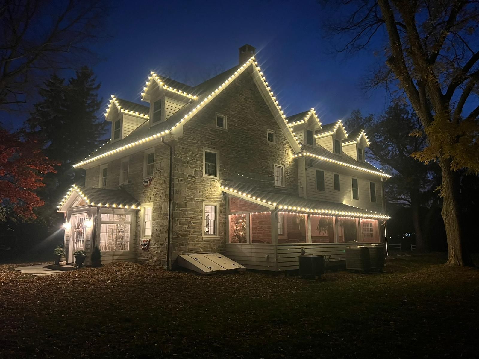 Stone house at night, lit with warm white string lights along the roof and porch.