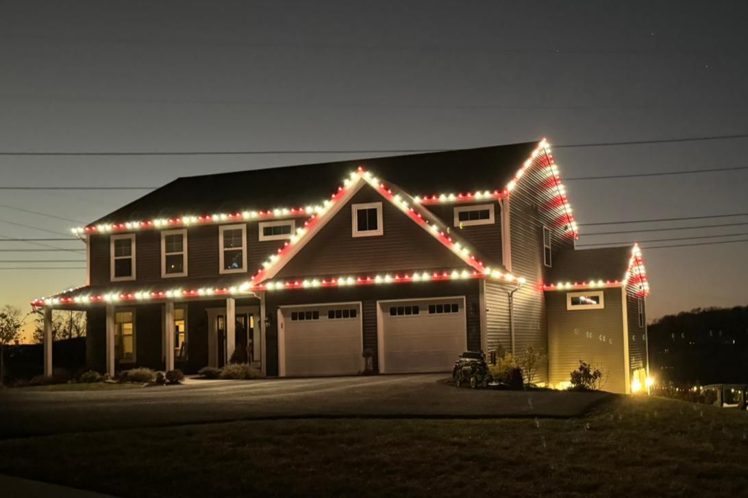 House decorated with red and white Christmas lights outlining the roof and windows at dusk.