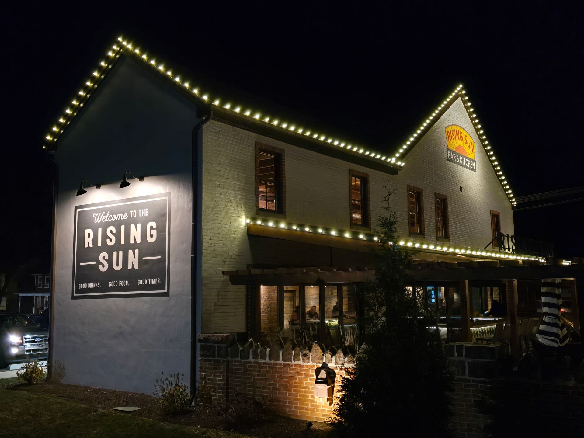Night view of Rising Sun restaurant with string lights. A sign welcomes visitors.