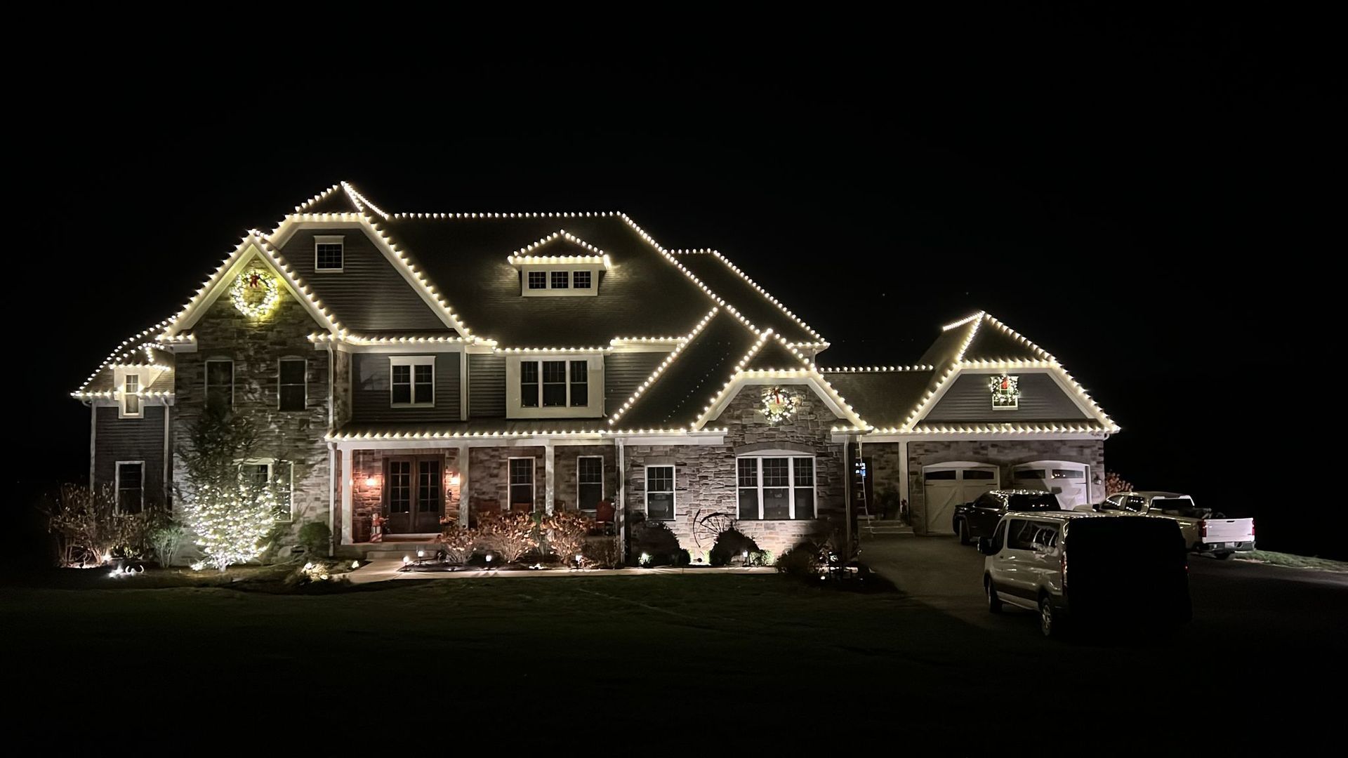 A large house at night, illuminated with white Christmas lights, with a dark background.