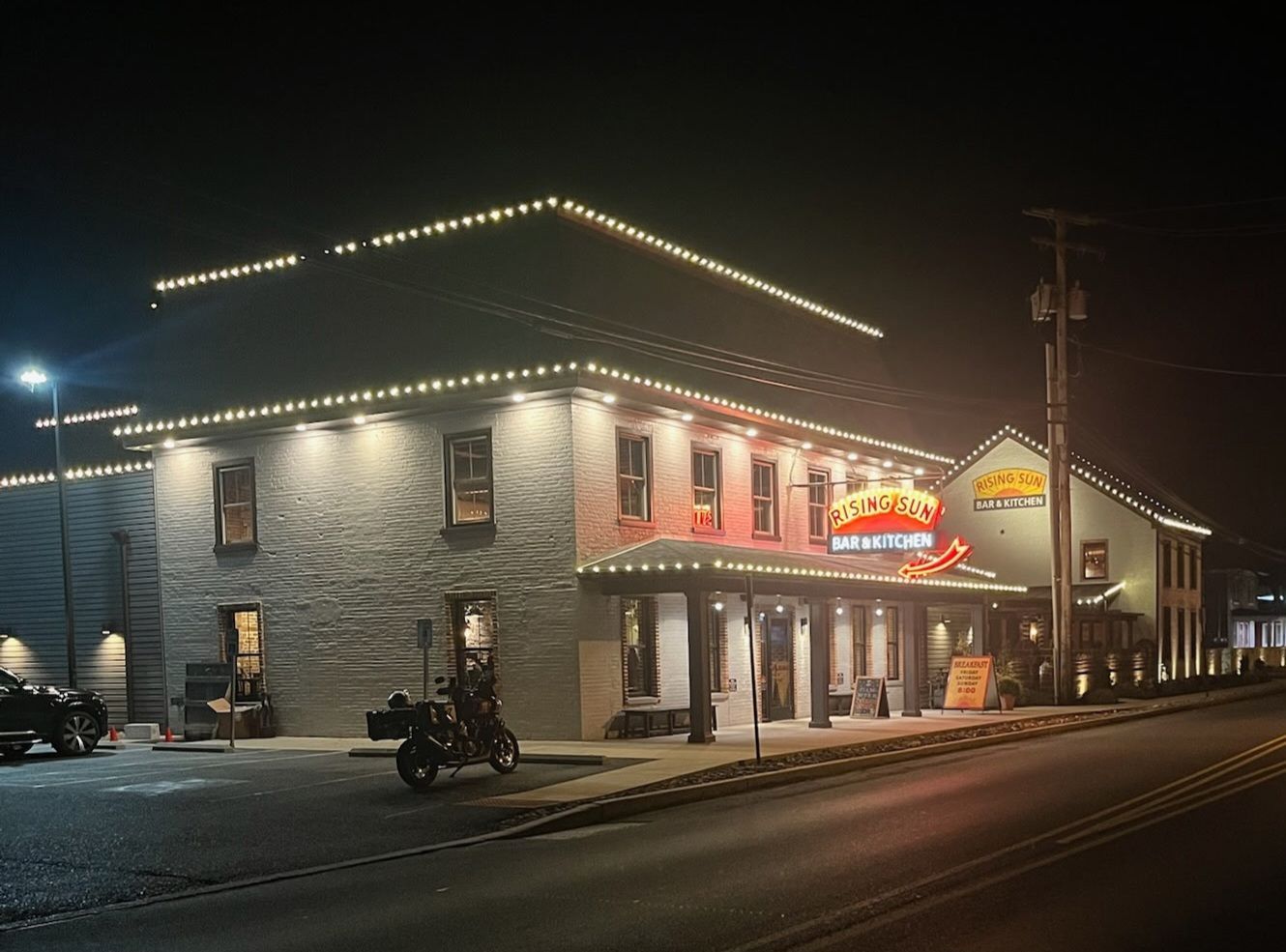 Night view of a two-story building with string lights, a restaurant with red neon sign and a parked motorcycle on the street.