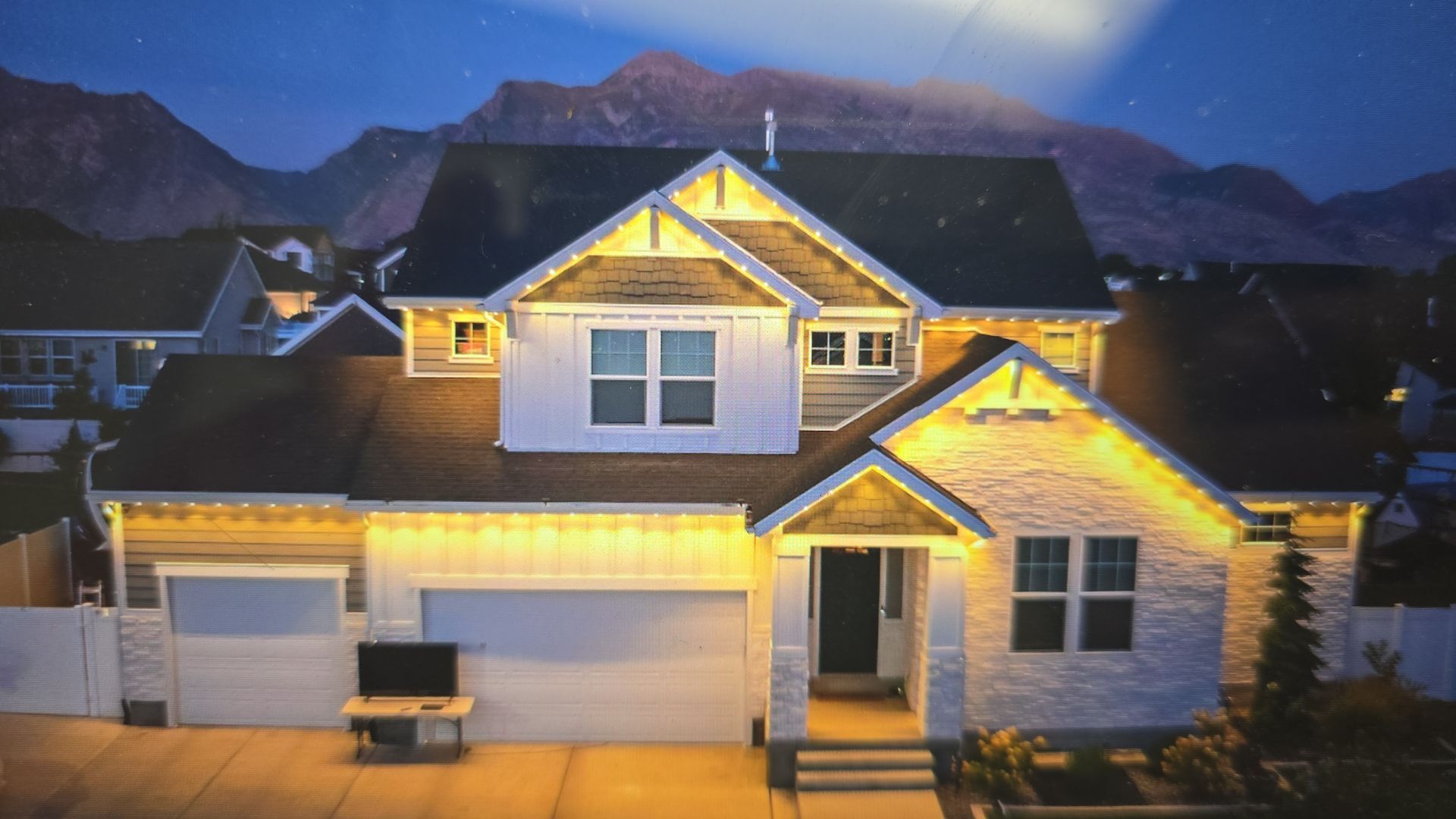 A two-story house at night, lit up, with a mountain backdrop.