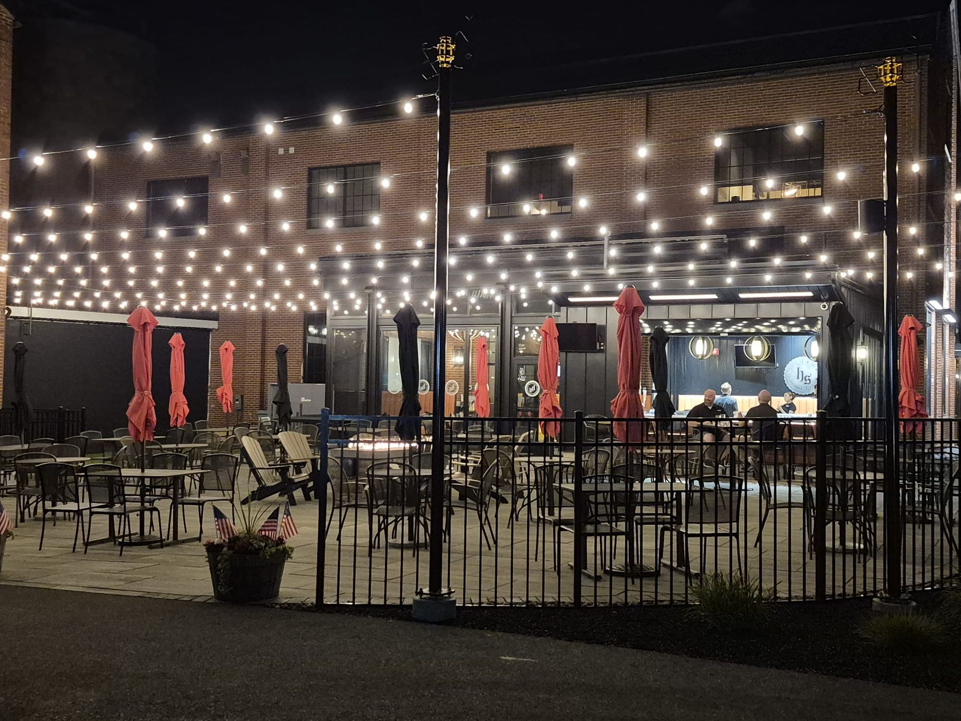 Outdoor patio at night with string lights and closed red umbrellas.