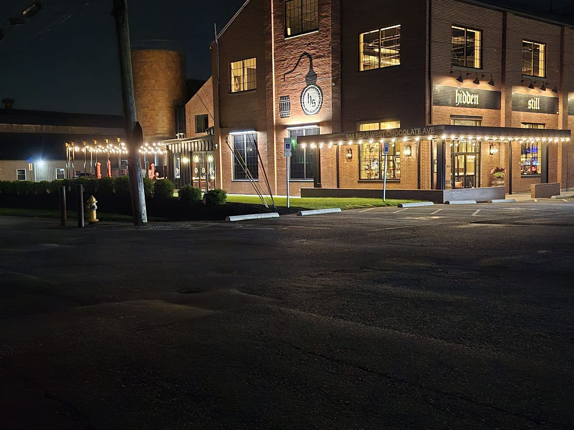 Brick building at night with string lights, a clock, and a small patio.