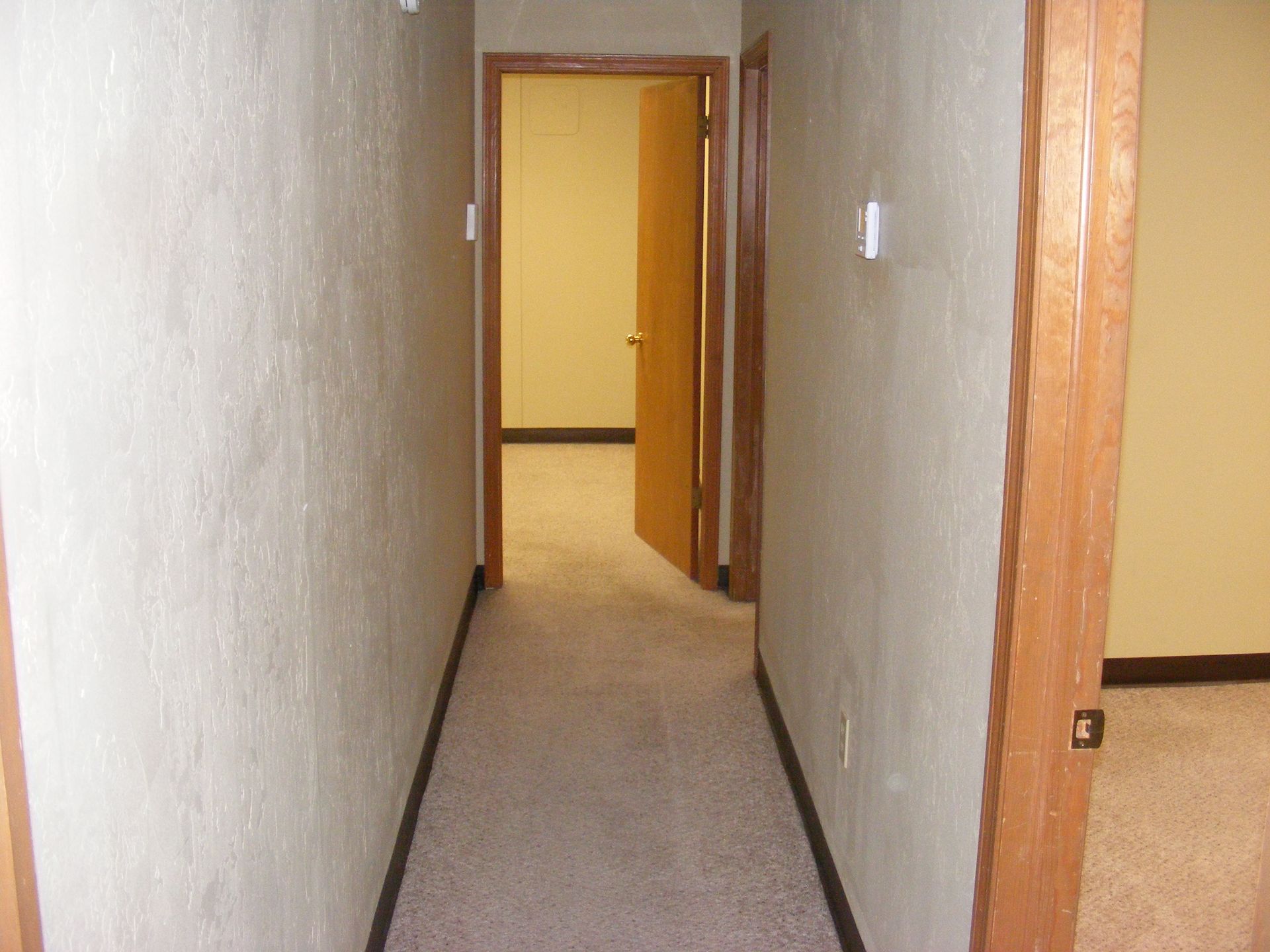 A long hallway with a door leading to a room.