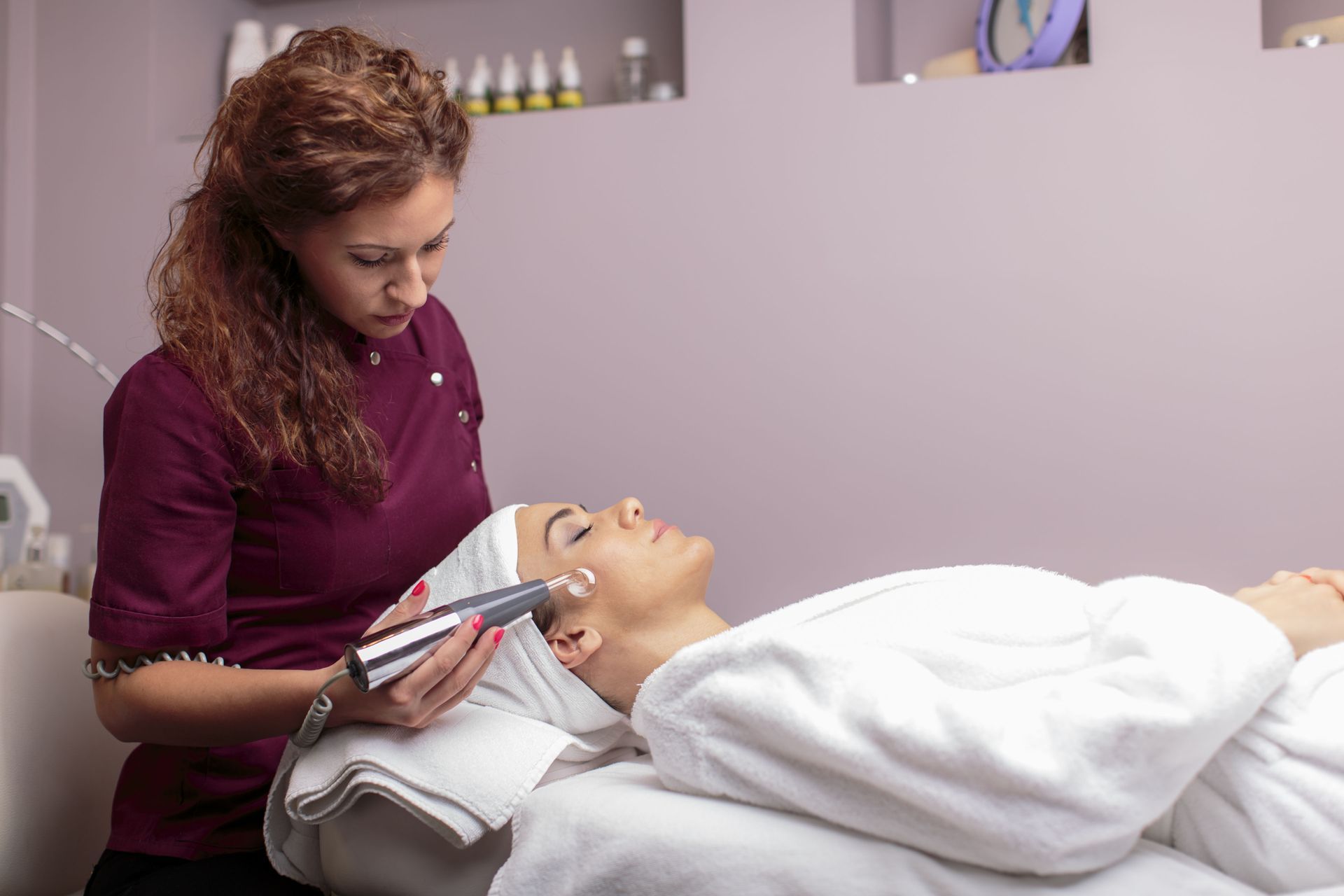 Woman receiving facial treatment in a spa, therapist holding a device near her face.