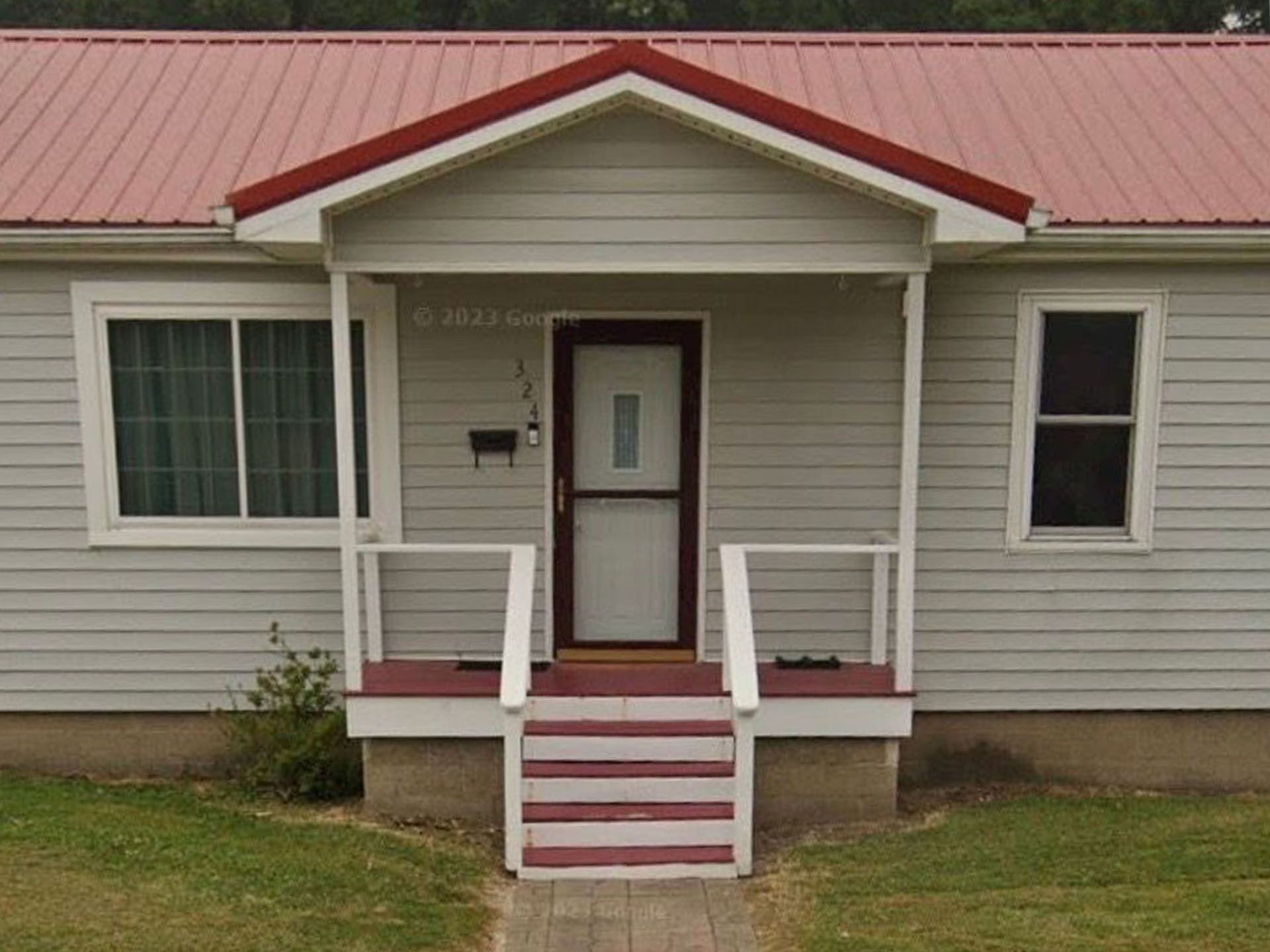Small beige house with a red roof, centered front door, porch, and red-and-white steps.