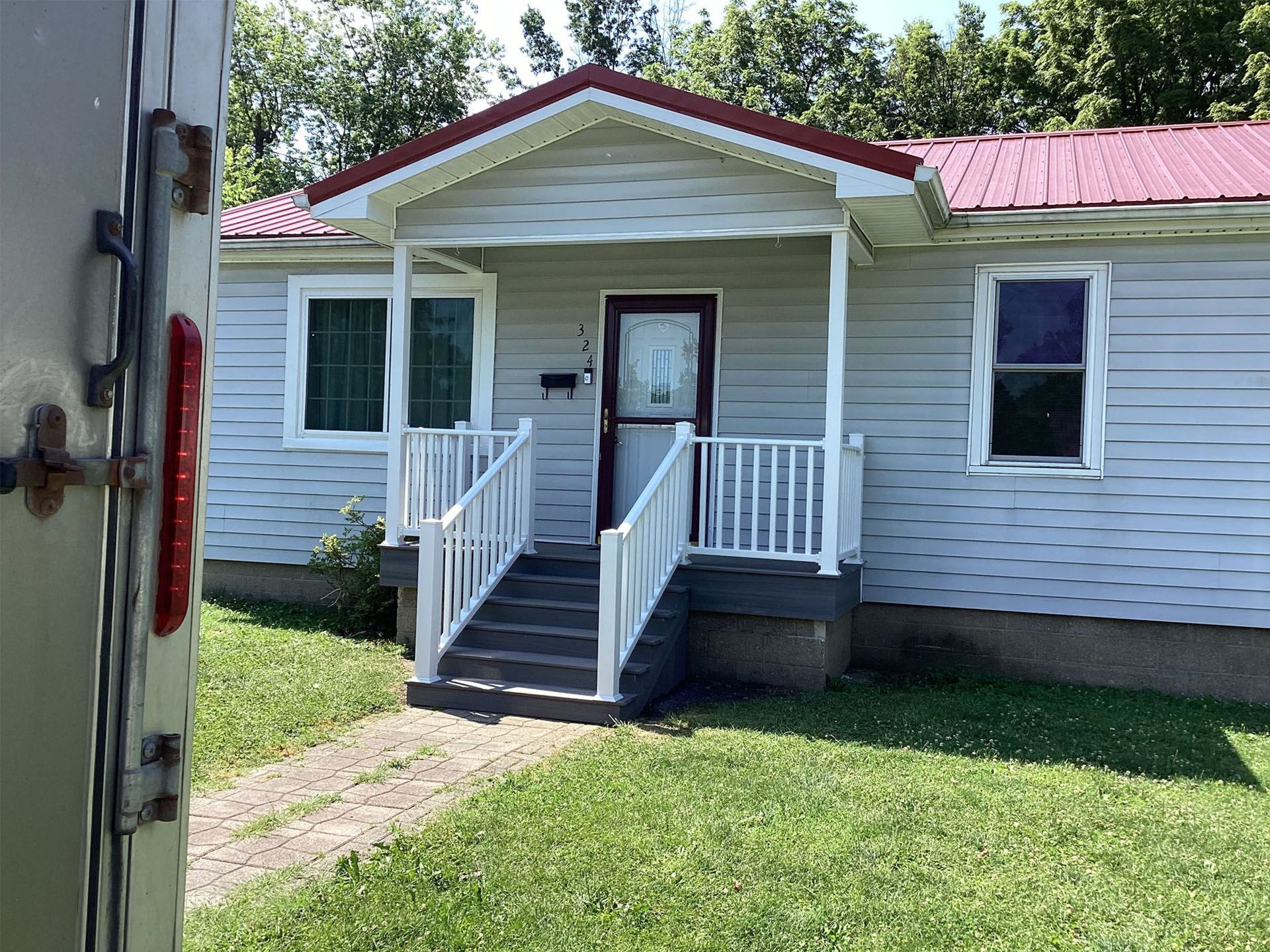 Small white house with a red roof, front porch, and steps, viewed from the yard.