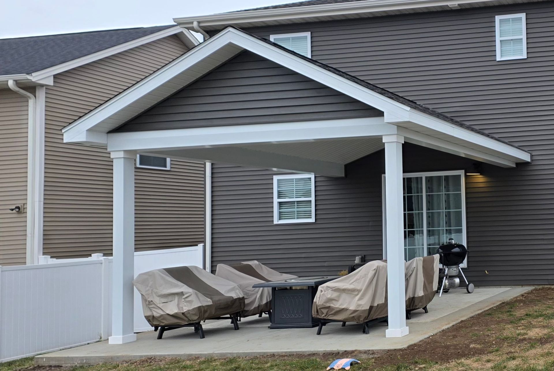 Covered patio with white posts, gray siding, and outdoor furniture beside a house