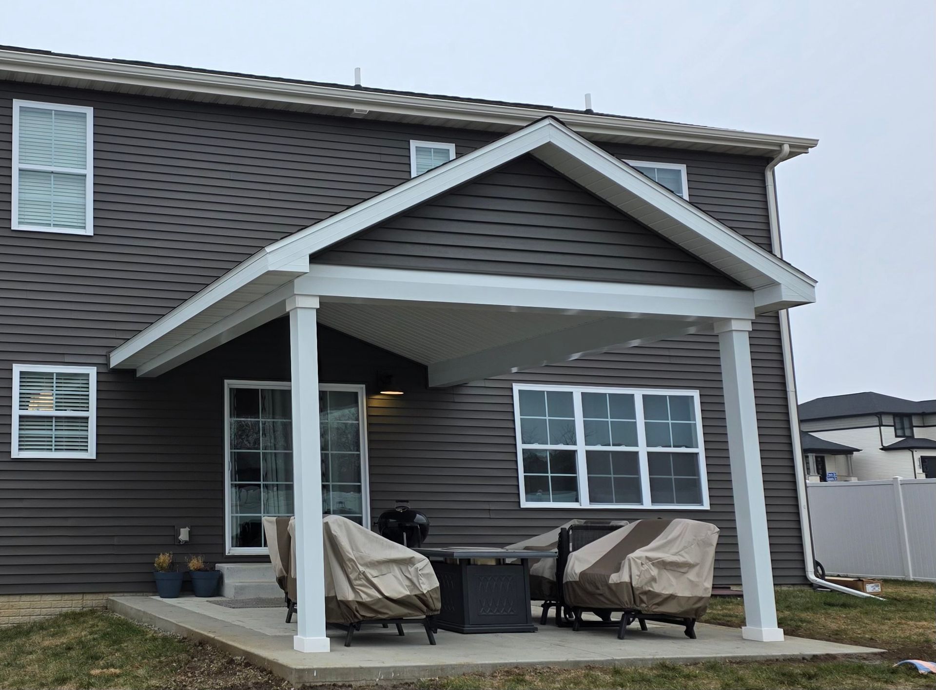 Back patio with white columns, covered seating, and dark gray siding on a house