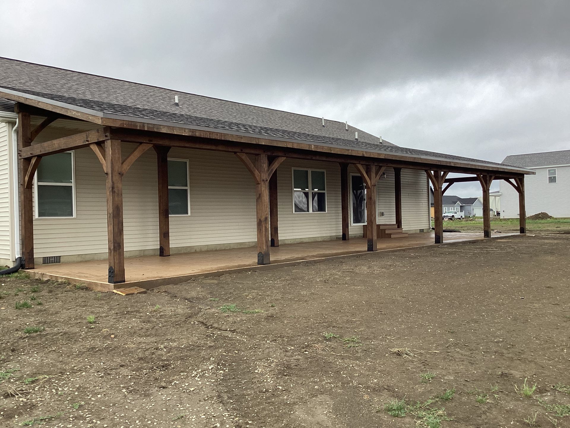 Rural wooden porch on a beige building under a cloudy sky, with bare dirt in the foreground.