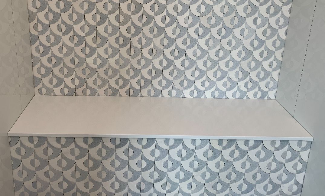 A white shelf is sitting in front of a wall with a pattern on it.