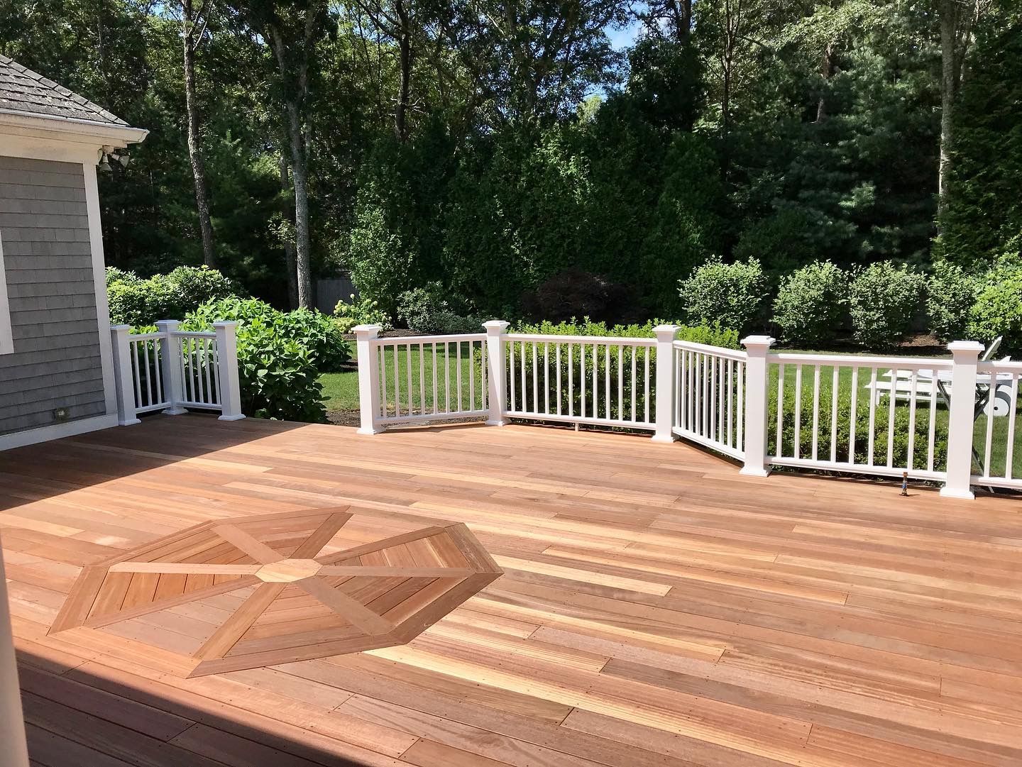 A wooden deck with a white railing and trees in the background