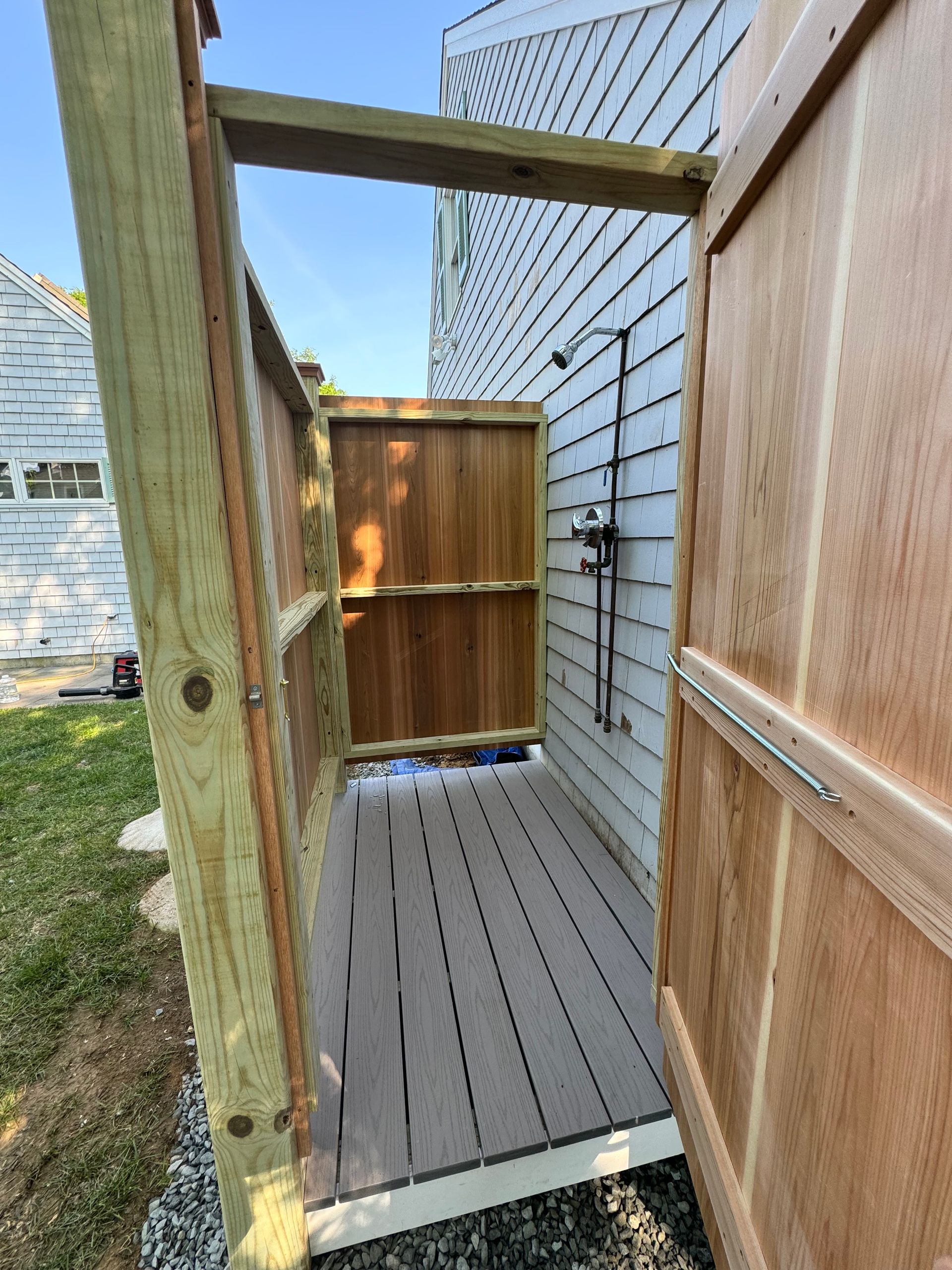 A wooden outdoor shower with a wooden door is built into the side of a house