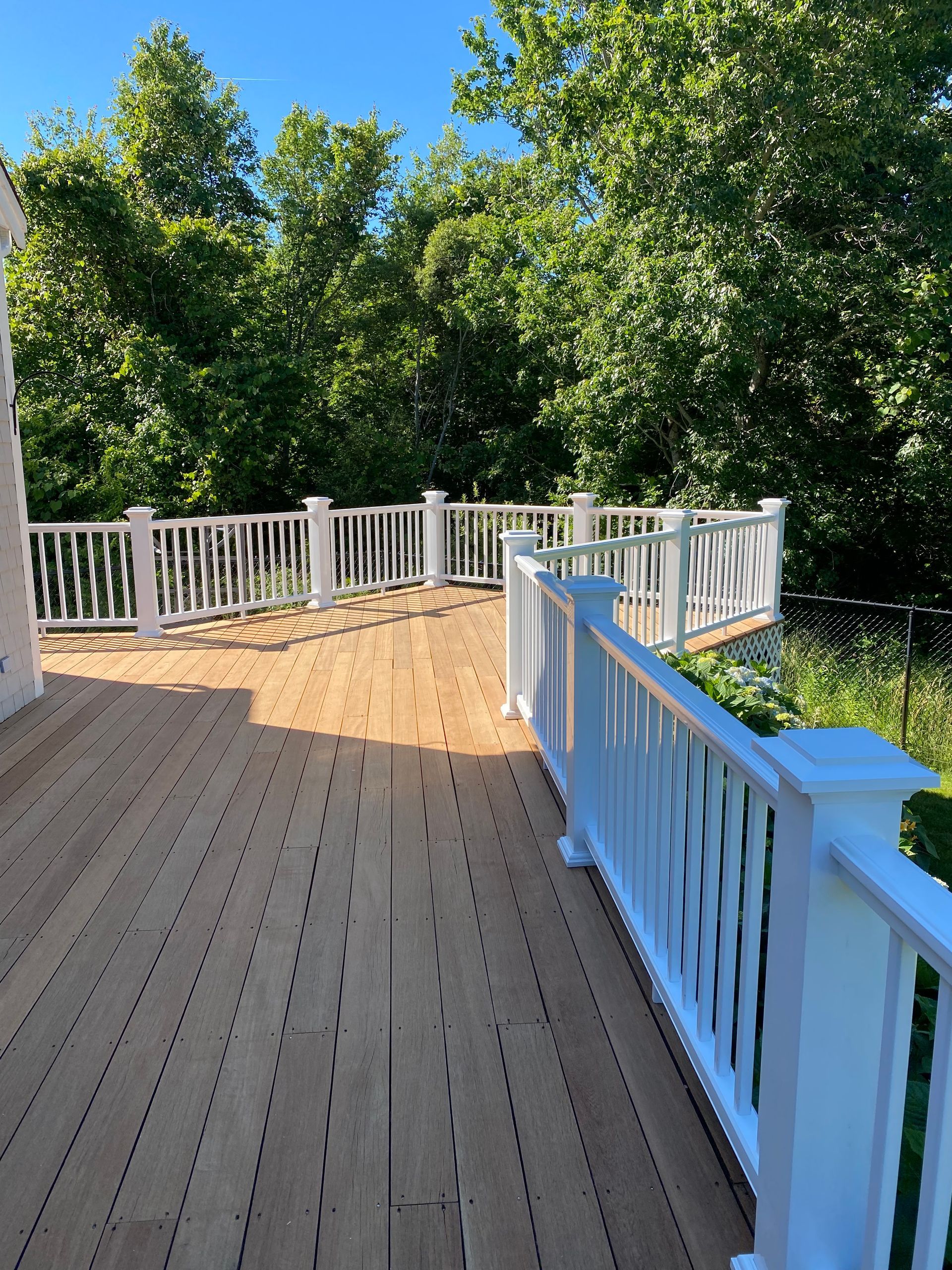 A wooden deck with a white railing and trees in the background