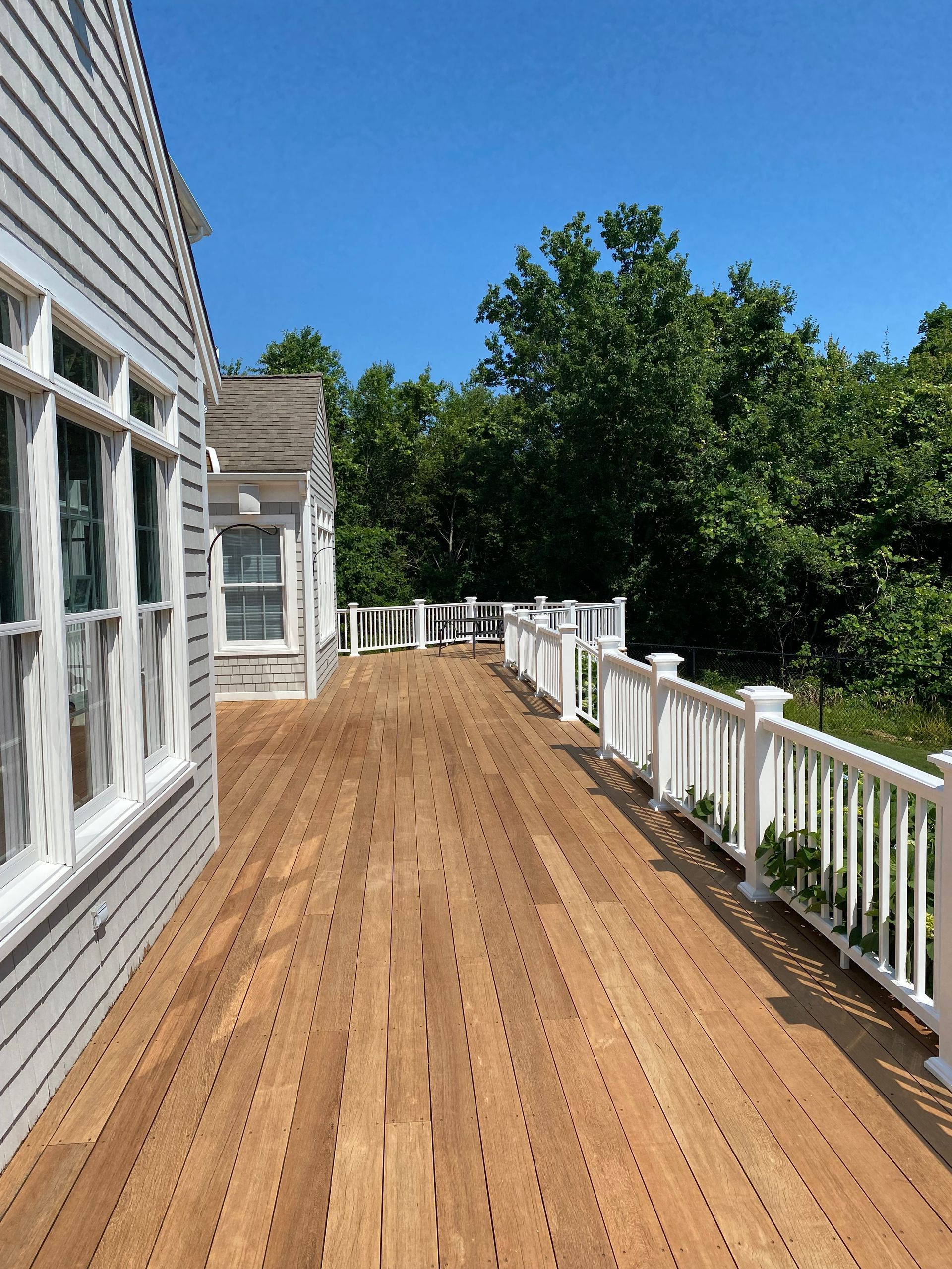 A wooden deck with a white railing and a white house in the background