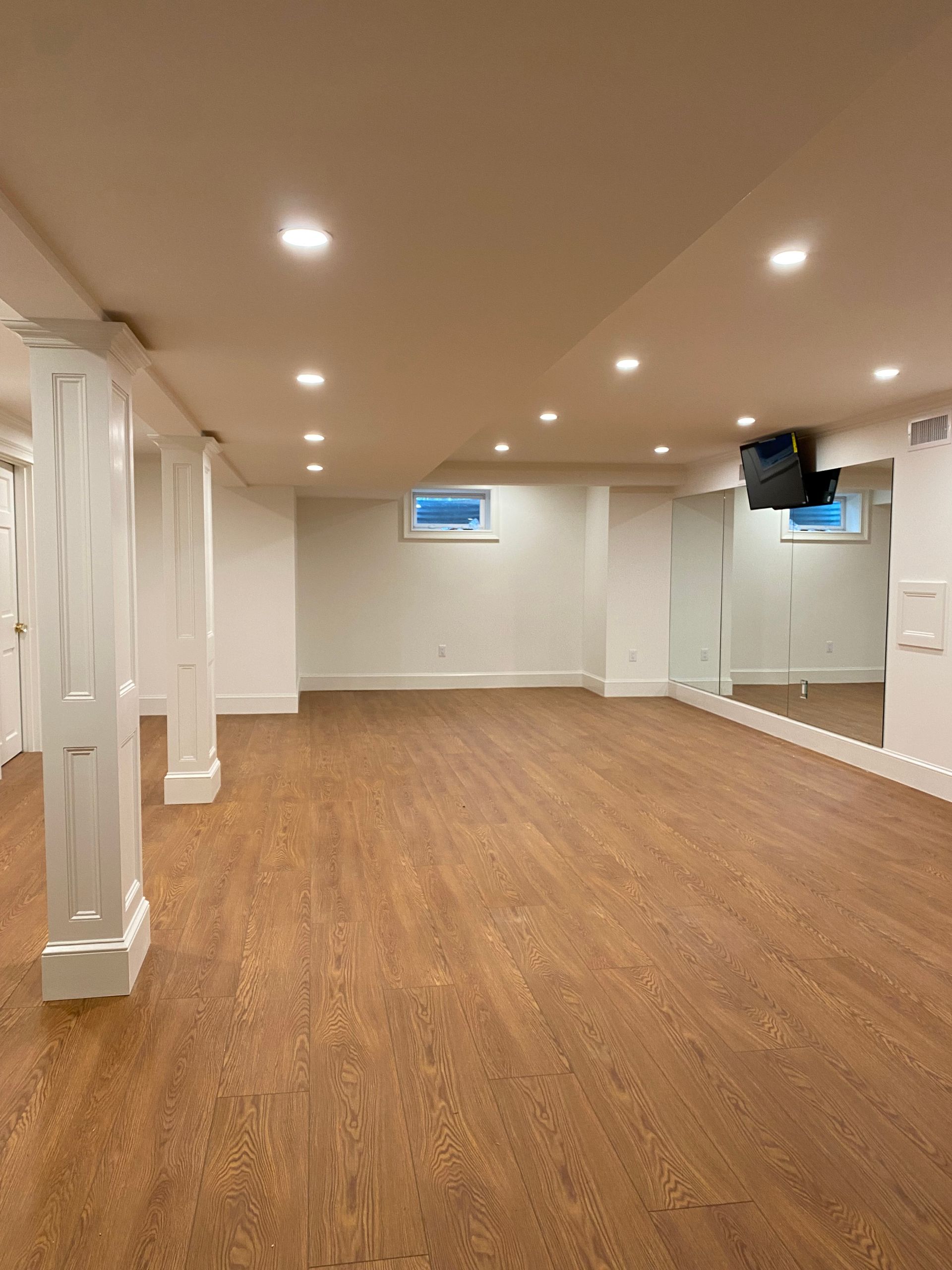 An empty basement with hardwood floors and a large mirror