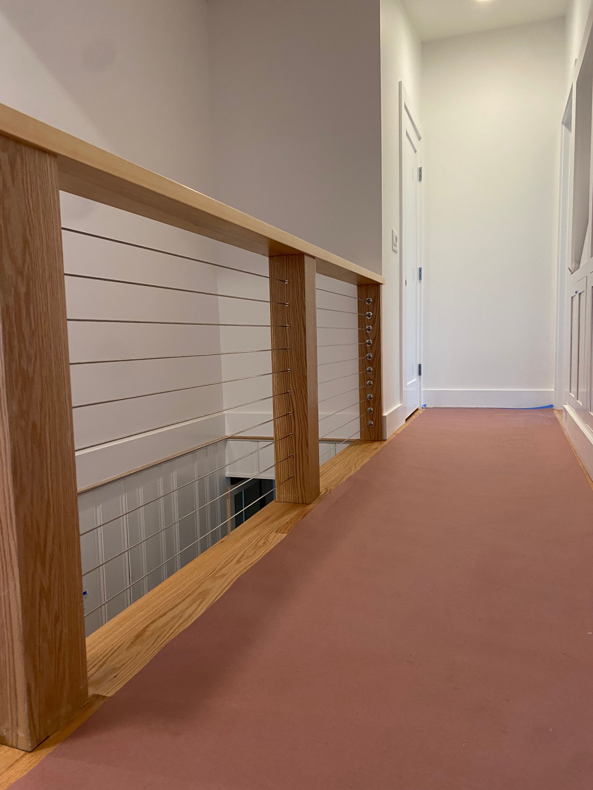 A hallway with a wooden railing and a pink carpet
