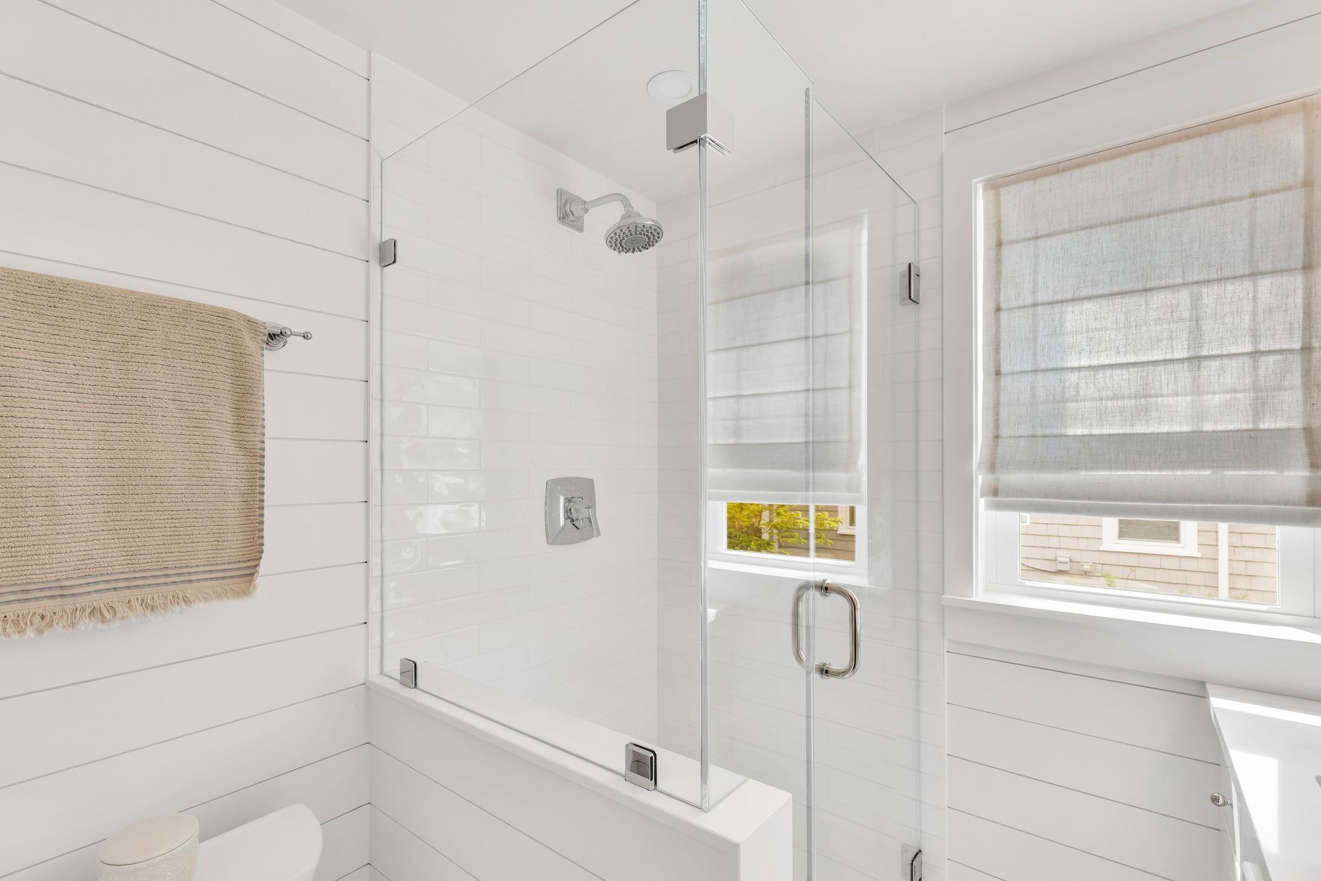 Bright white bathroom with a glass shower, towel bar, and window light