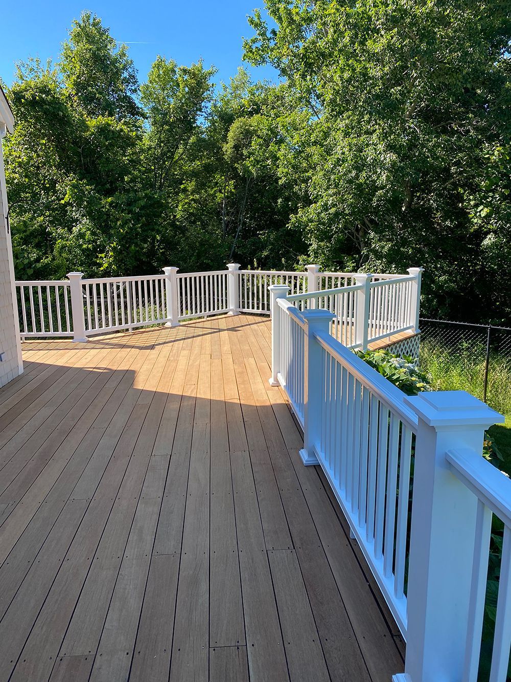 A wooden deck with a white railing and trees in the background