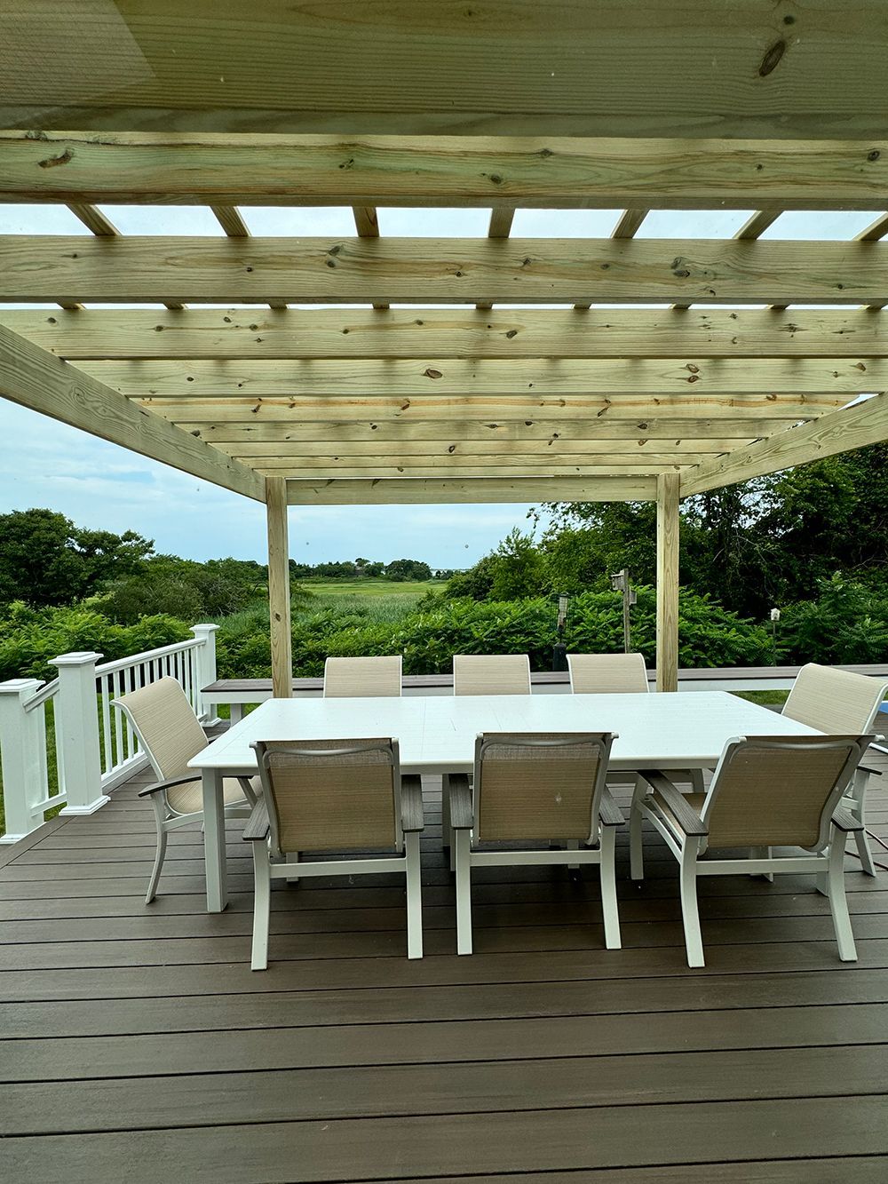 A wooden deck with a table and chairs under a pergola.