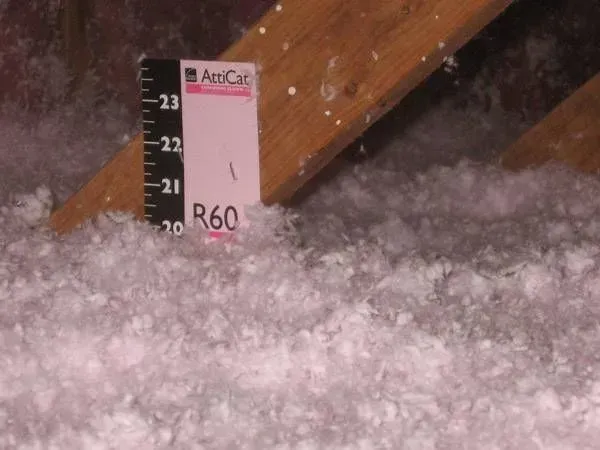 Attic insulation with a ruler showing an R-60 rating against a wooden beam.