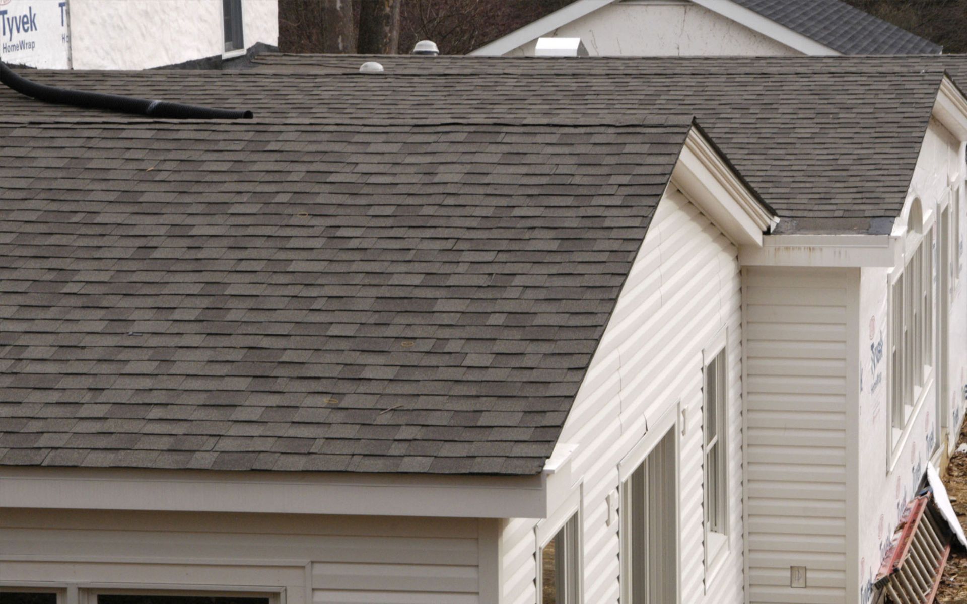 Gray shingle roof on a white-sided building with gutters and several windows.