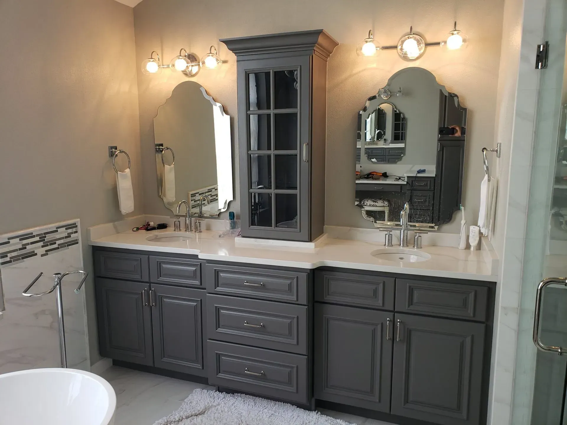 Bathroom with gray vanity, two mirrors, cabinet, and white countertops.