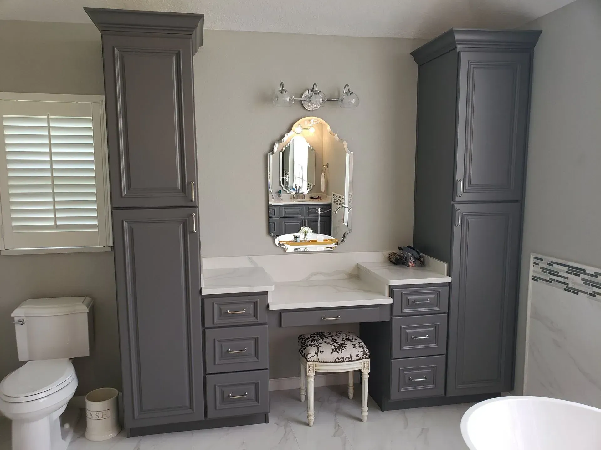 Gray bathroom vanity with storage cabinets, marble countertop, and decorative mirror.
