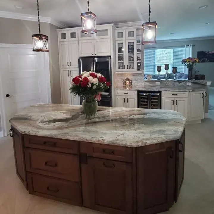 A kitchen with a brown island, white cabinets, and granite countertops. Flowers on the island.