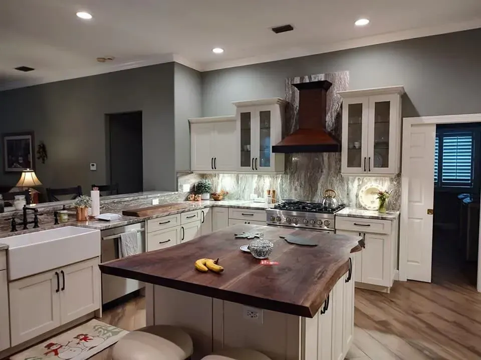 A kitchen with white cabinets, wood island, stainless steel appliances, and a dark brown range hood.