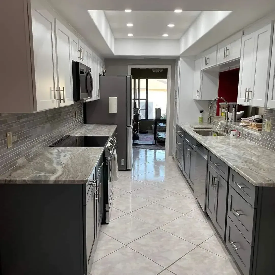 Modern galley kitchen with gray and white cabinets, granite countertops, and tiled backsplash.