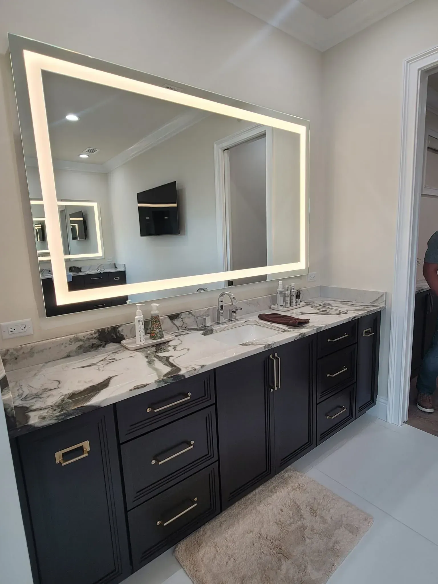 Bathroom vanity with illuminated mirror, black cabinets, granite countertop.