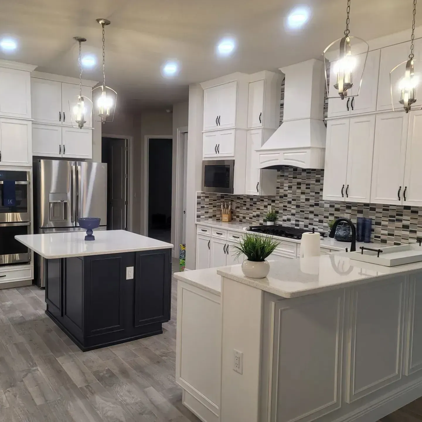 Modern white kitchen with dark blue island, stainless steel appliances, and wood flooring.
