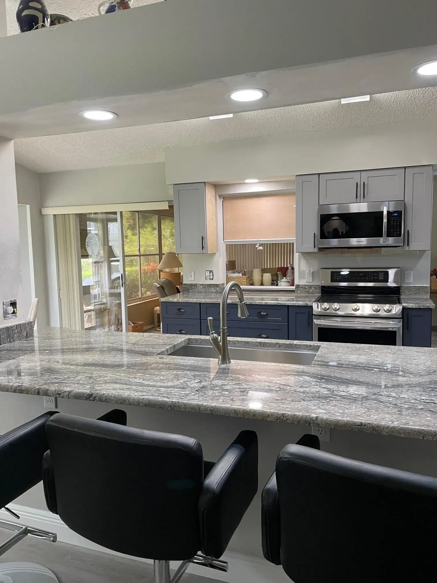 Kitchen with granite countertop, gray and blue cabinets, stainless steel appliances, and bar stools.