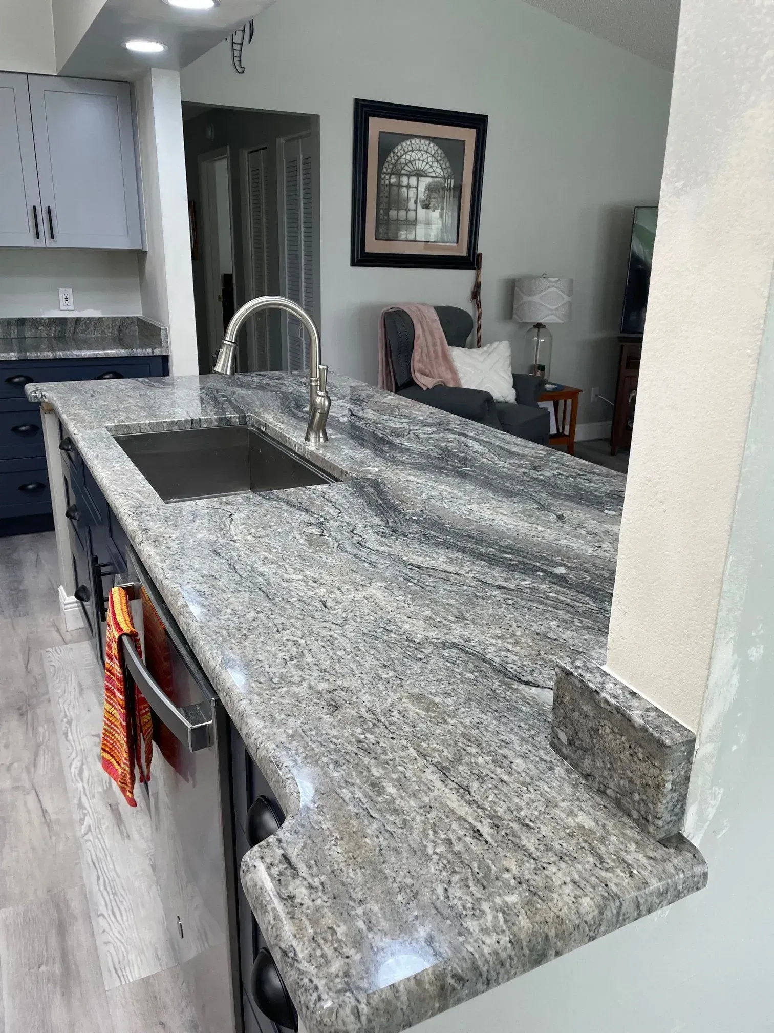 Kitchen island with granite countertop, sink, and faucet. Dark blue cabinets and a seating area in the background.