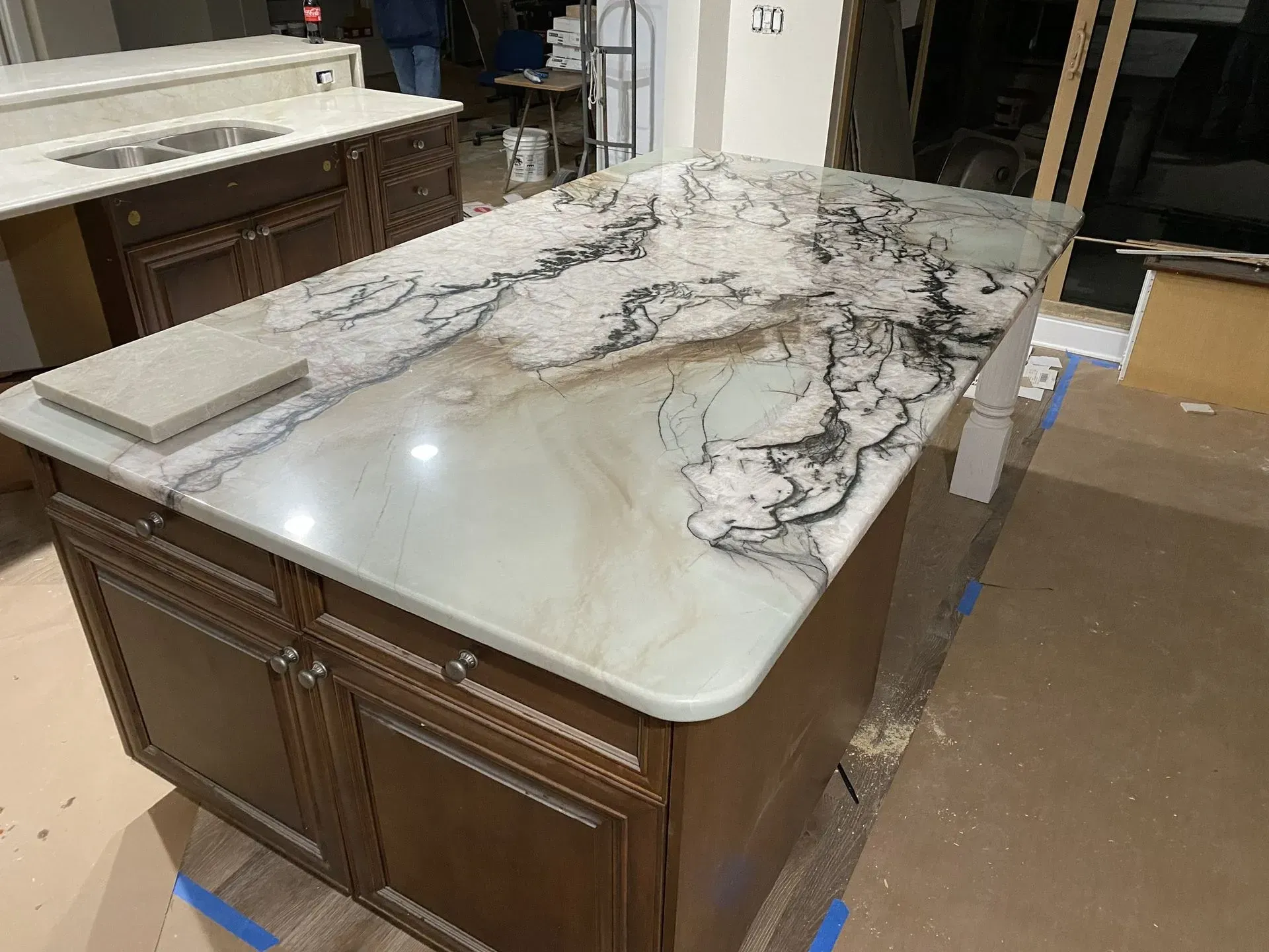 Kitchen island with light countertops, dark cabinetry, and white legs, in a room under construction.
